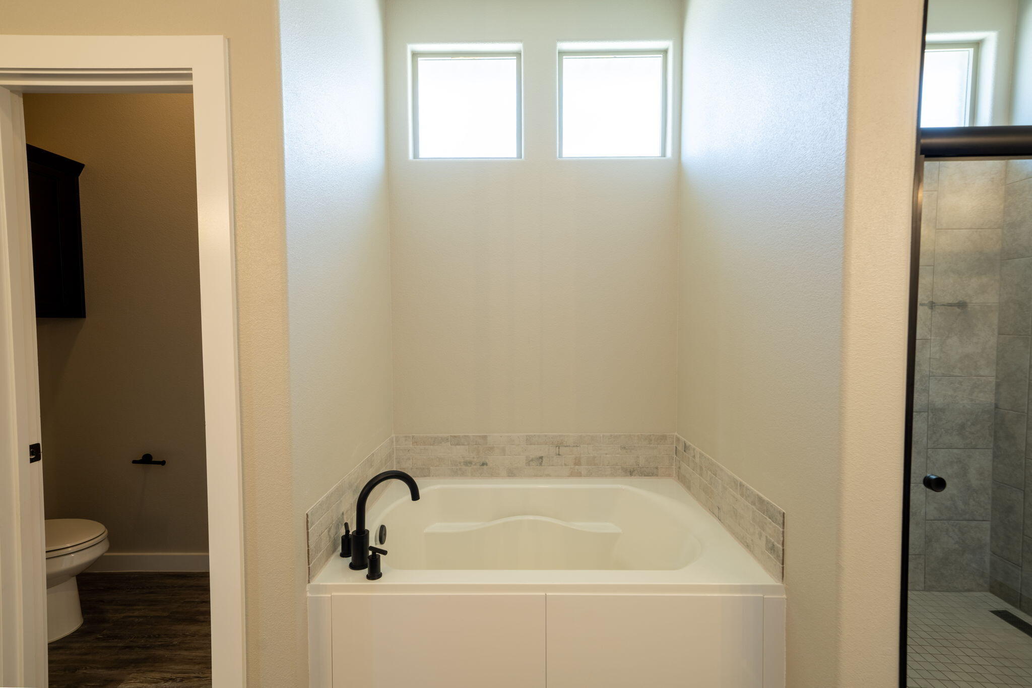 Bathroom soaking tub beneath two high windows, with a tiled glass shower beside it.