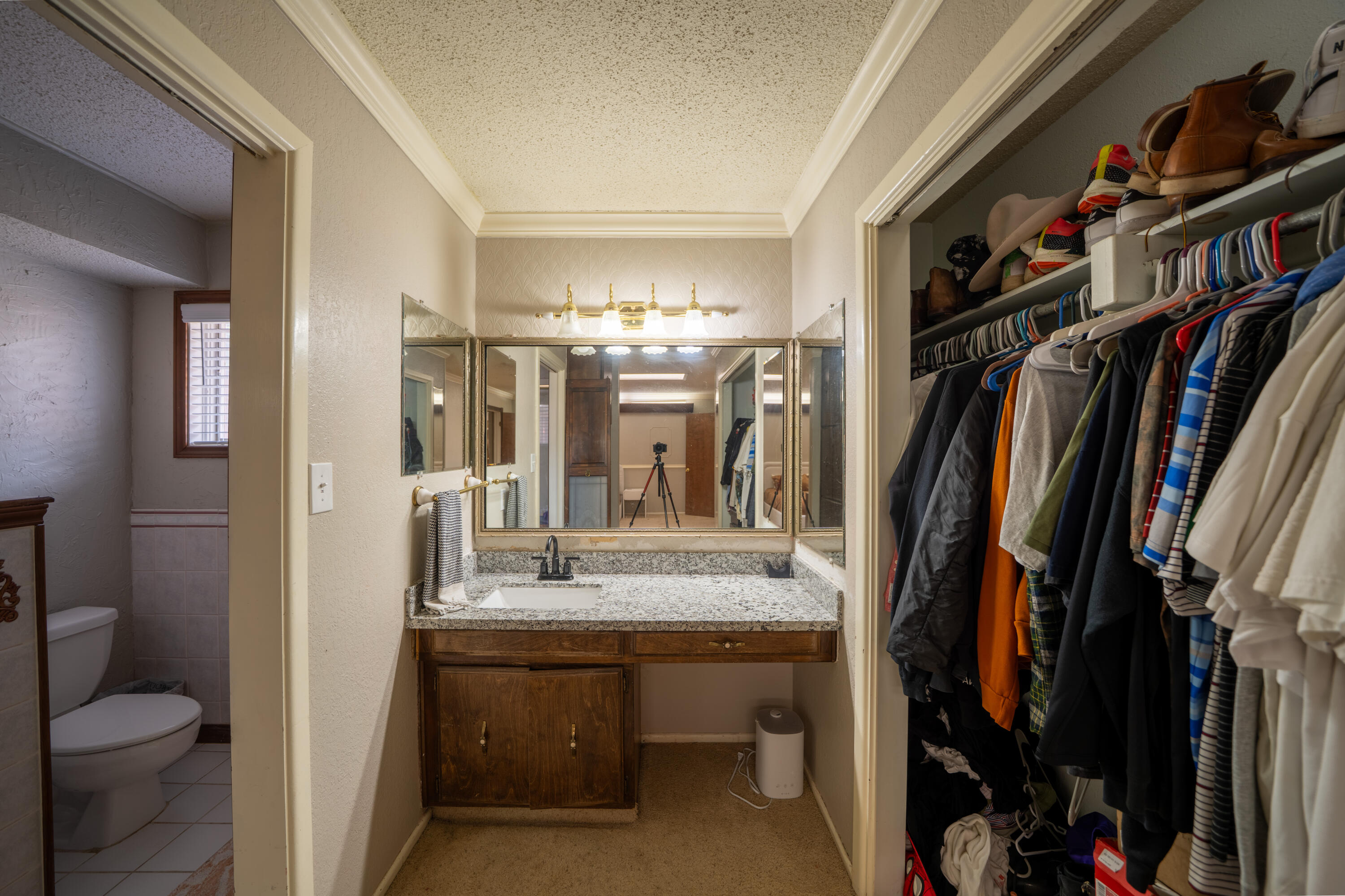 Bathroom vanity with mirrored cabinet, beside a walk-in closet filled with clothes and shoes.