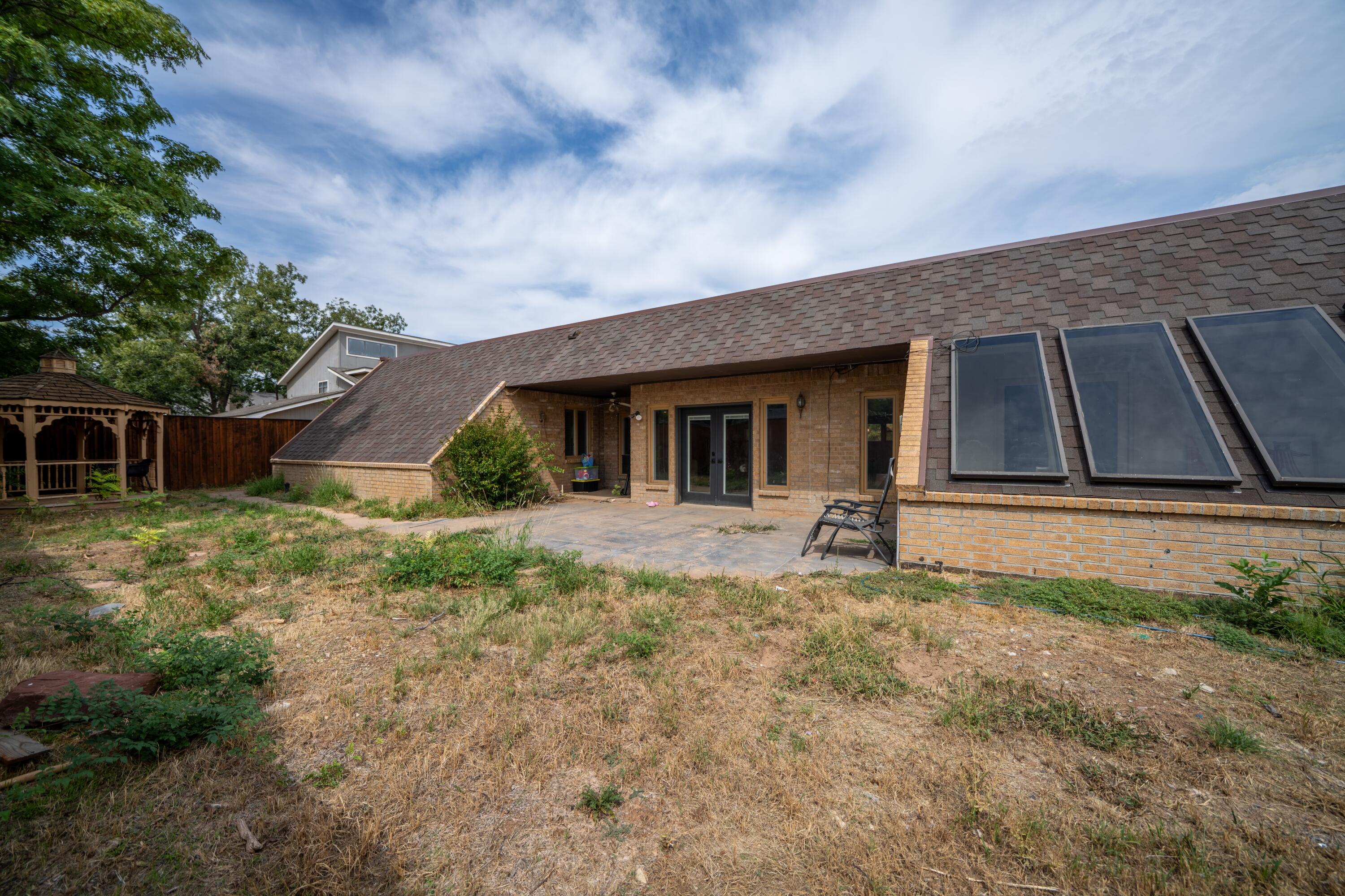 Brick house rear exterior with large roof windows, a paved patio, and a wooden gazebo.