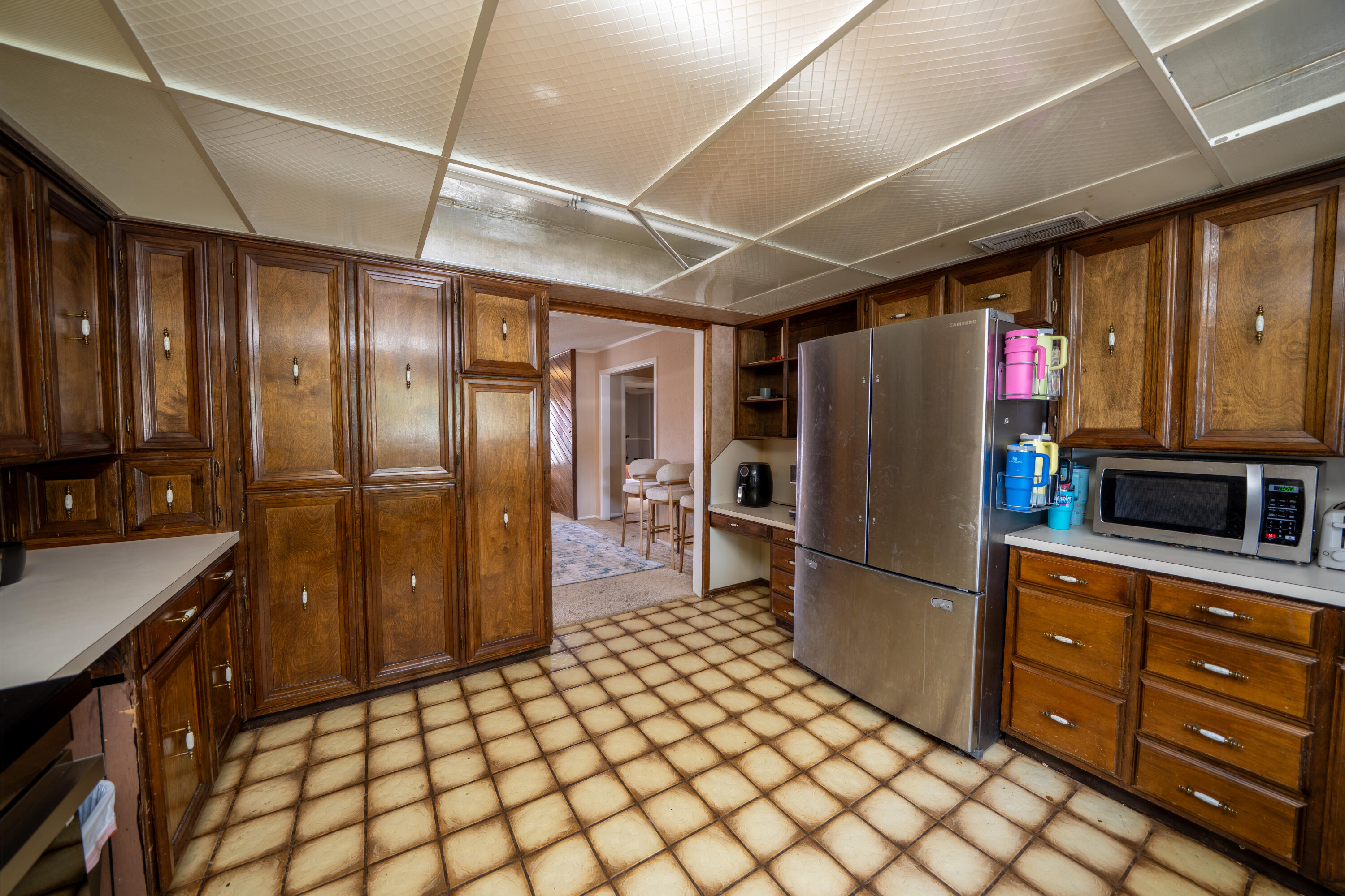Kitchen with extensive dark wood cabinets, square tile flooring, and a stainless steel refrigerator.