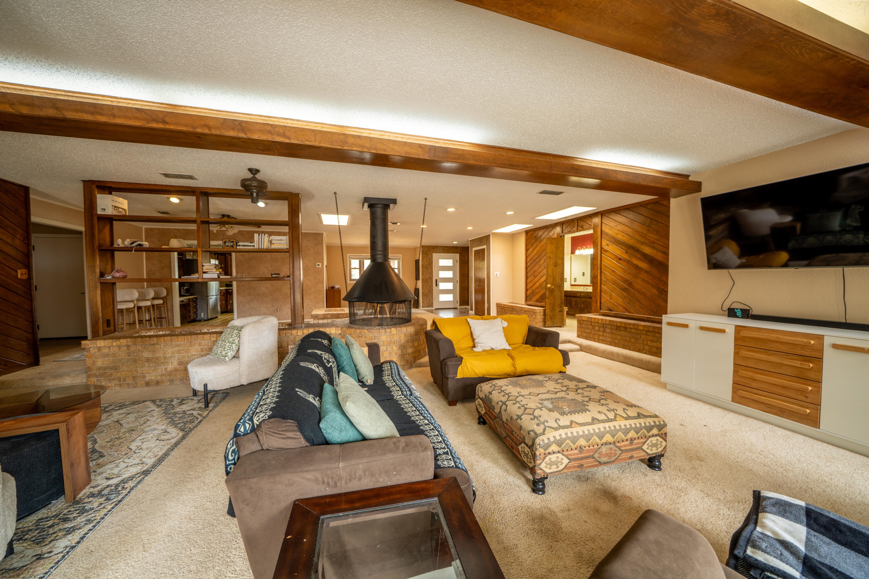 Living room with exposed wood beams, a suspended fireplace, built-in shelving, and a yellow loveseat.