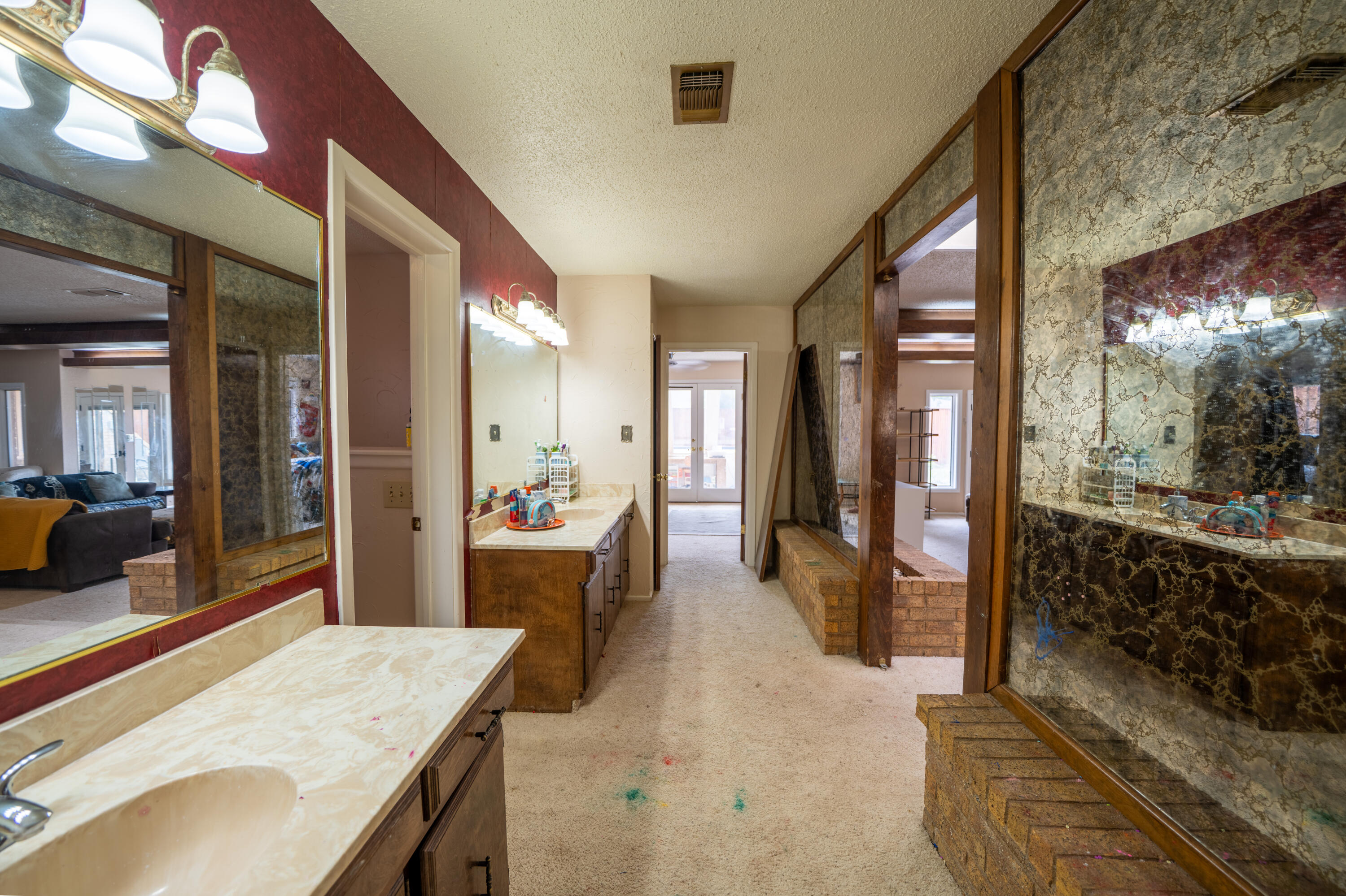 Bathroom vanity area with long countertops, wood-framed mirrors, and a carpeted passage to glass doors.