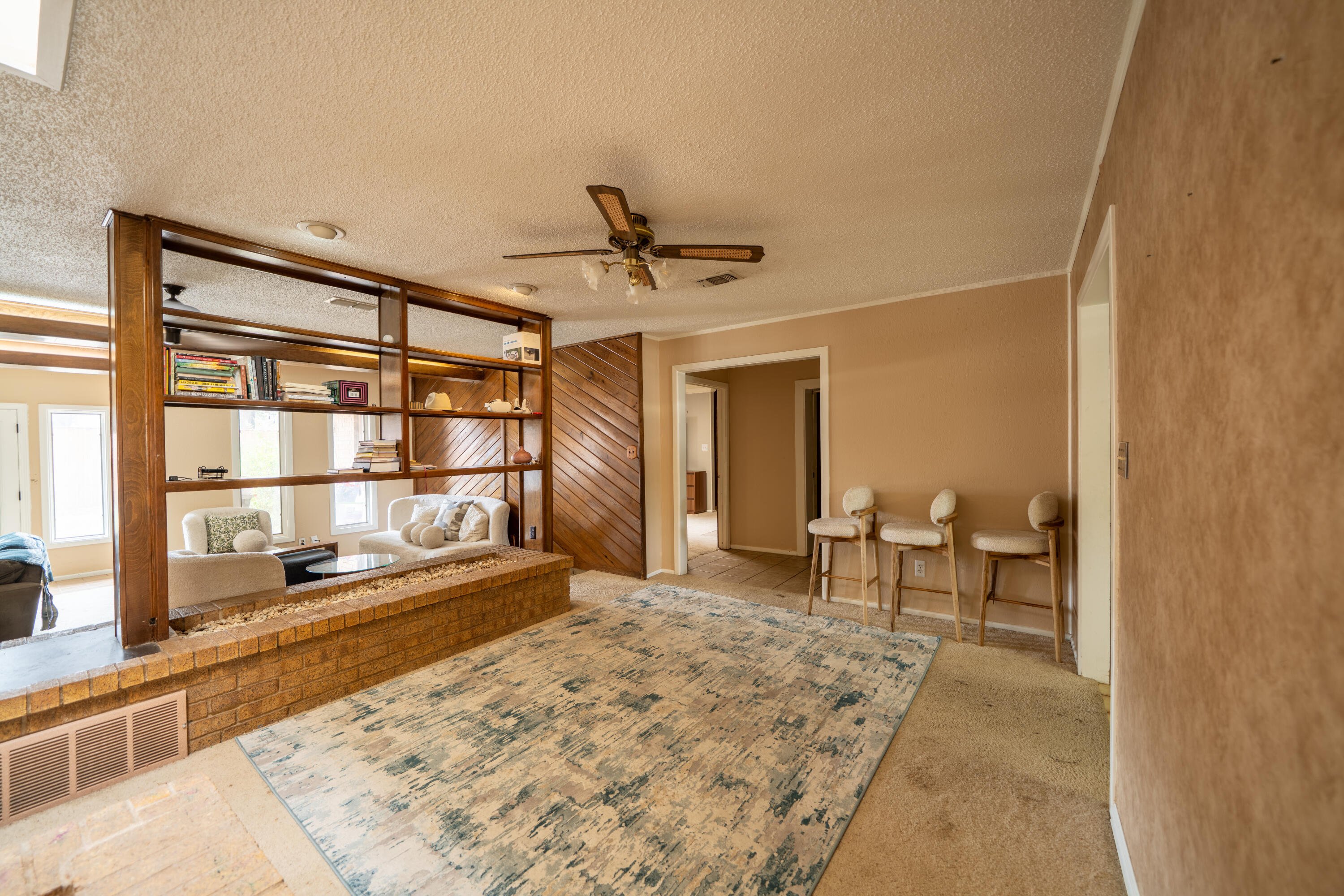Living room with open wood shelving, a brick half-wall, and three barstools.