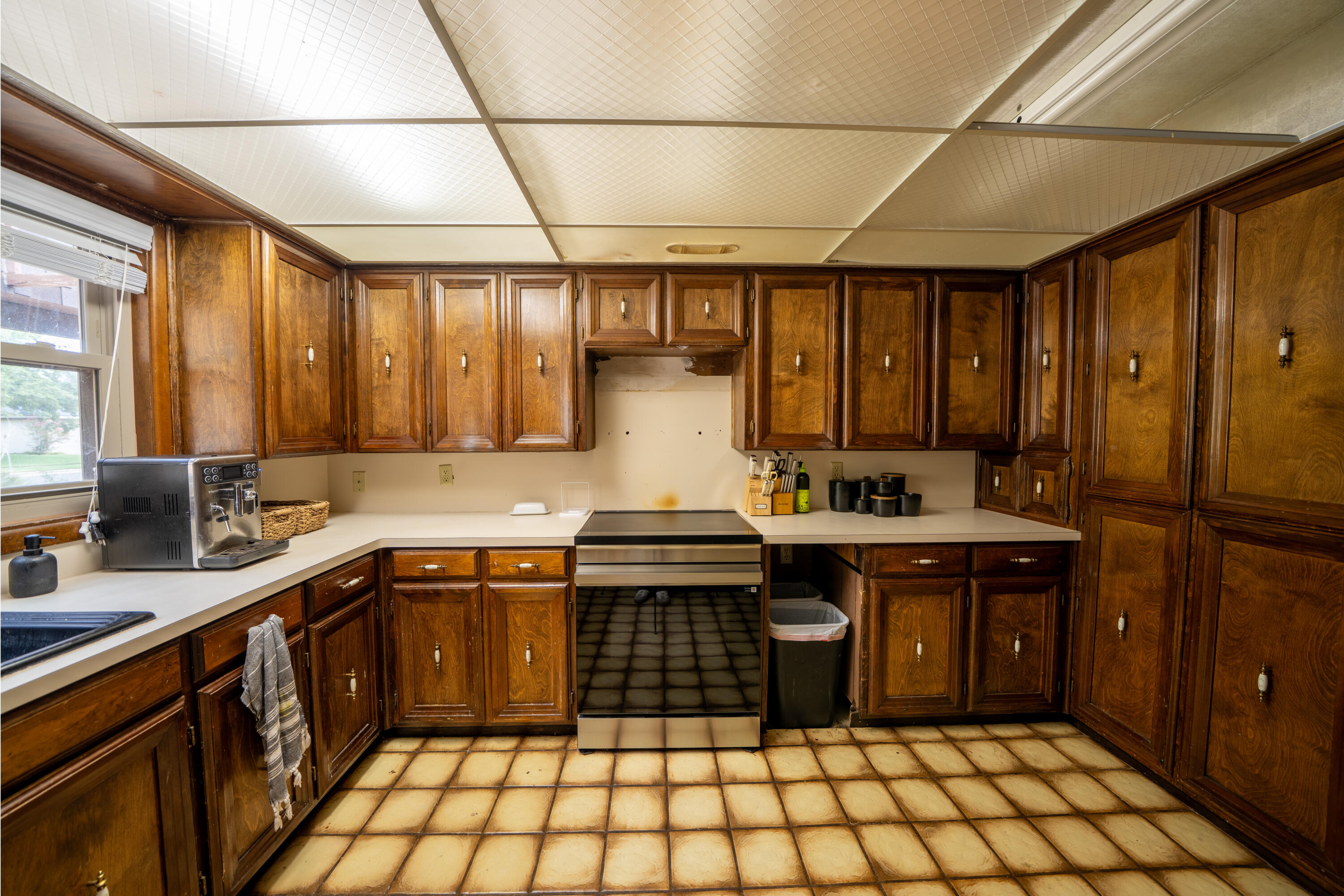 Kitchen with dark wood cabinetry, a central range, cream counters, and a tan tiled floor.