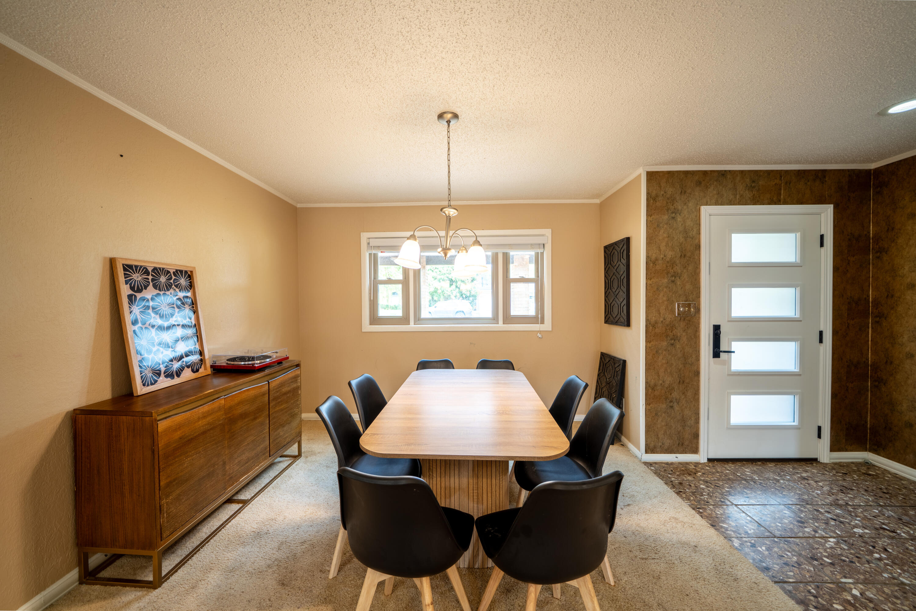 Dining room with a long wooden table, black chairs, sideboard, and frosted-glass exterior door.