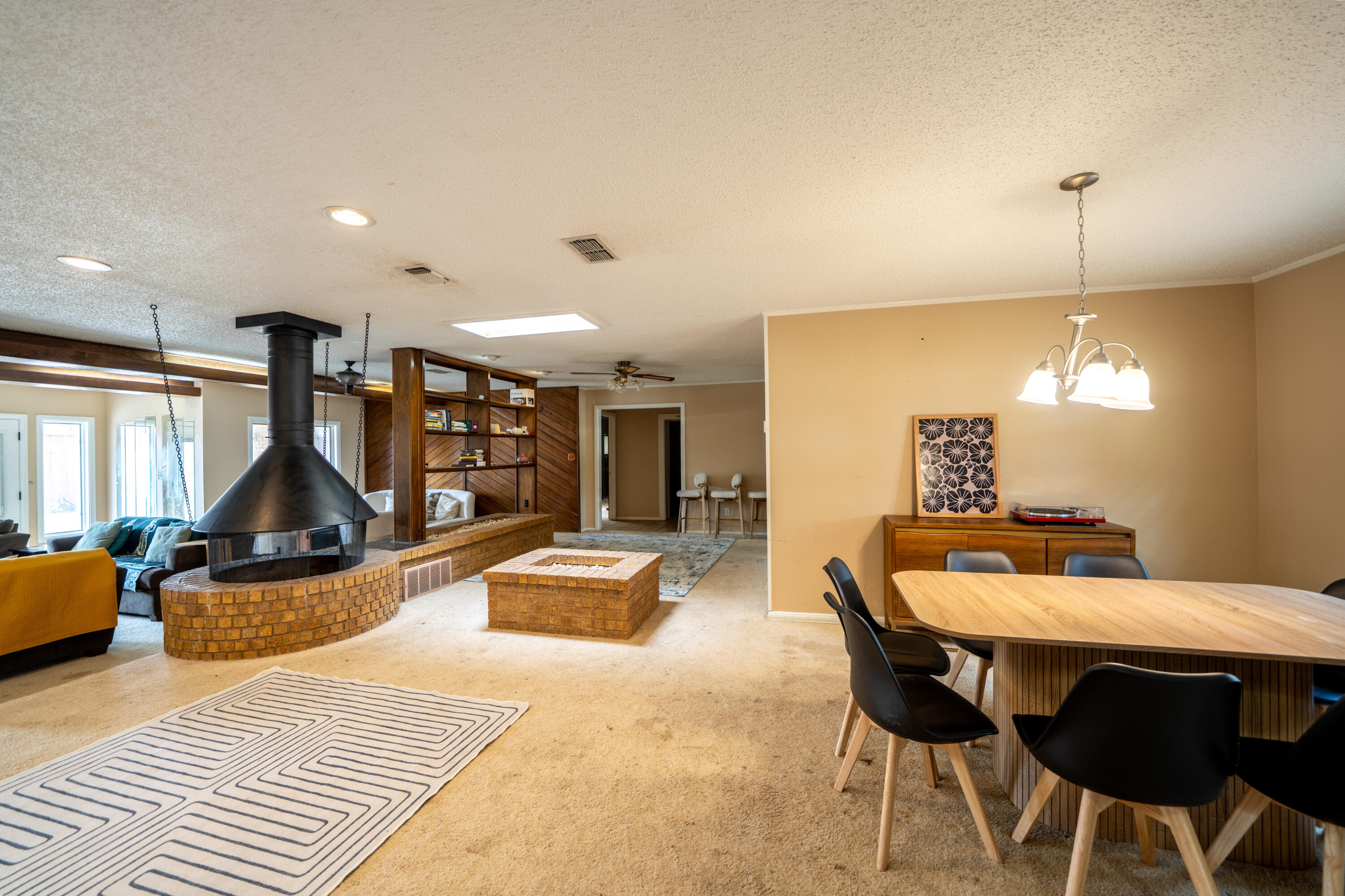 Open-plan living and dining room with a suspended fireplace above a brick hearth and a wood dining table.