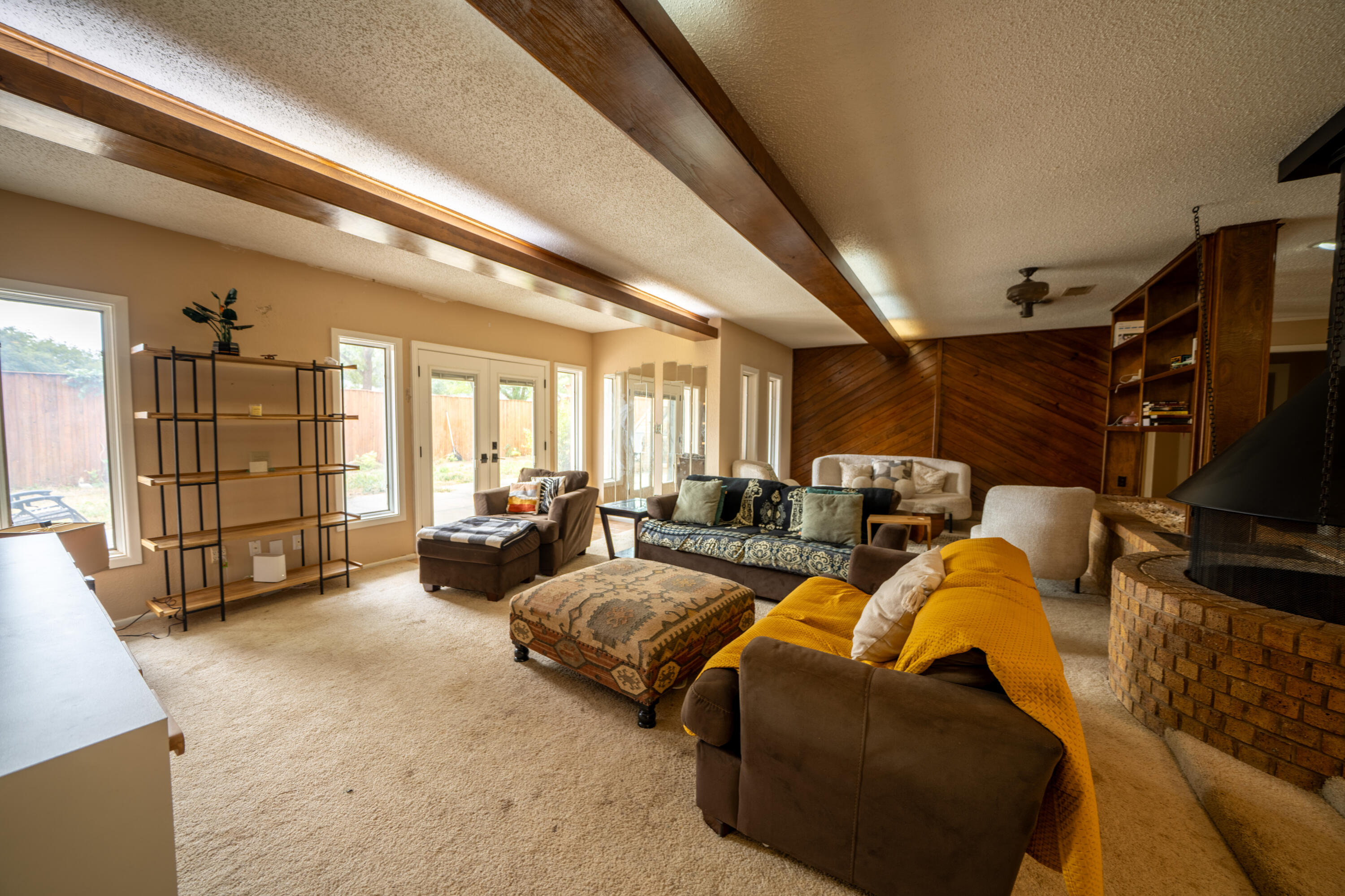 Furnished living room with exposed ceiling beams, brick fireplace, and wood-paneled accent wall.