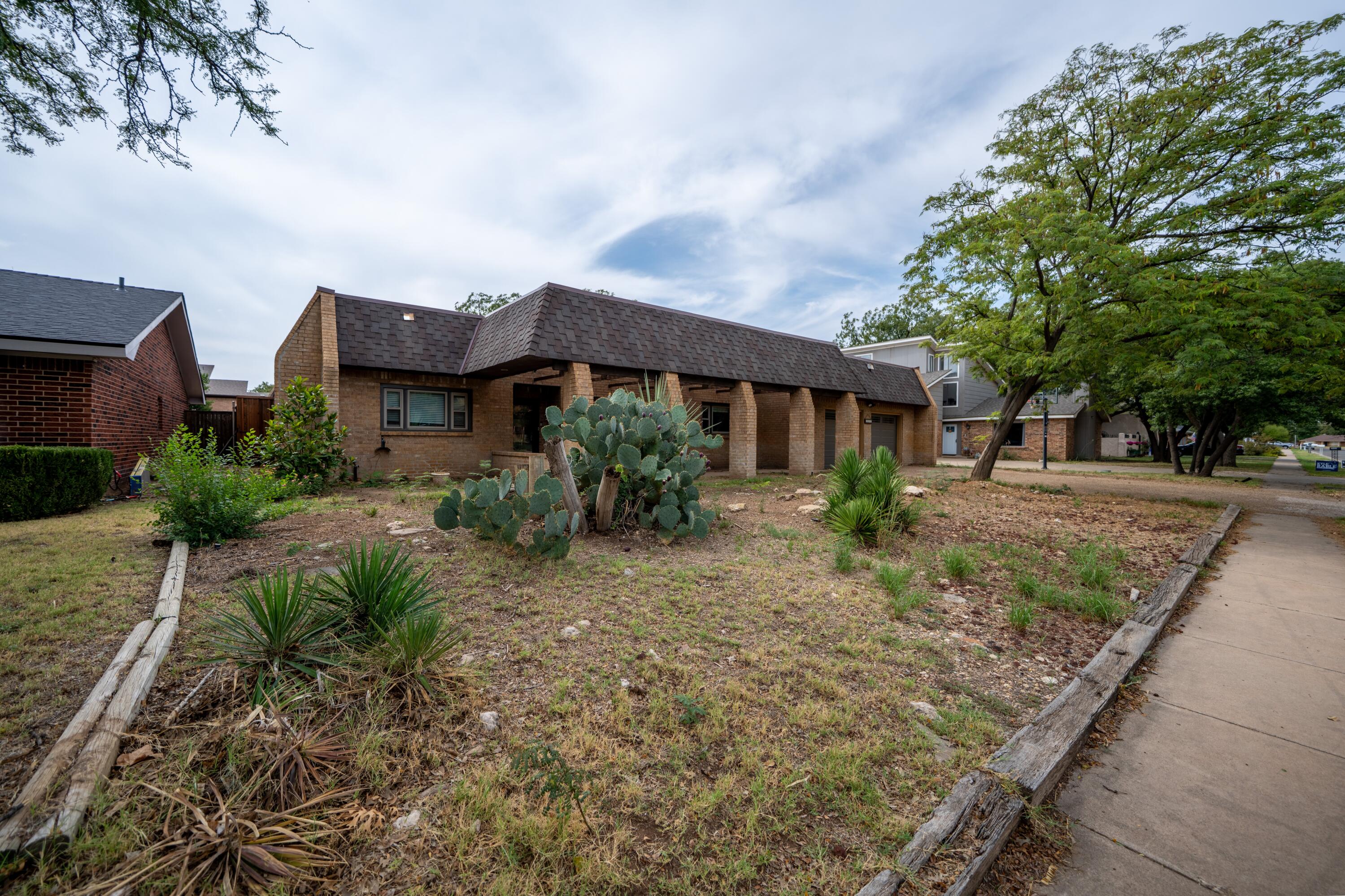 Single-story brick home with a deep covered porch and cactus landscaping beside the sidewalk.