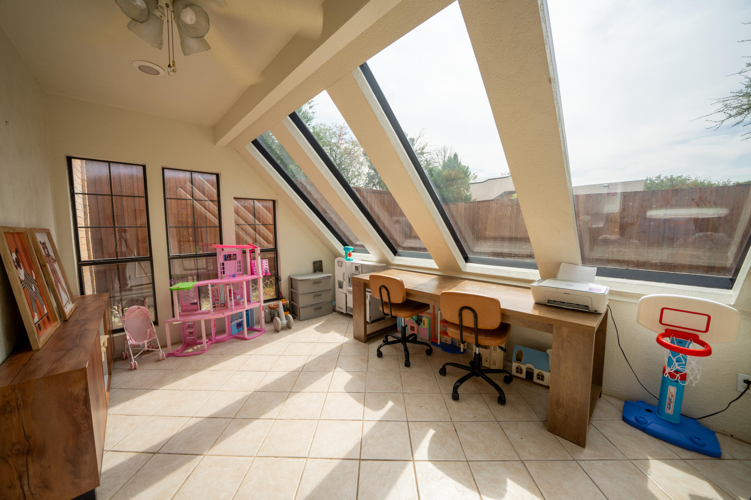 Playroom and study with dramatic slanted windows, a long desk, and children’s toys.