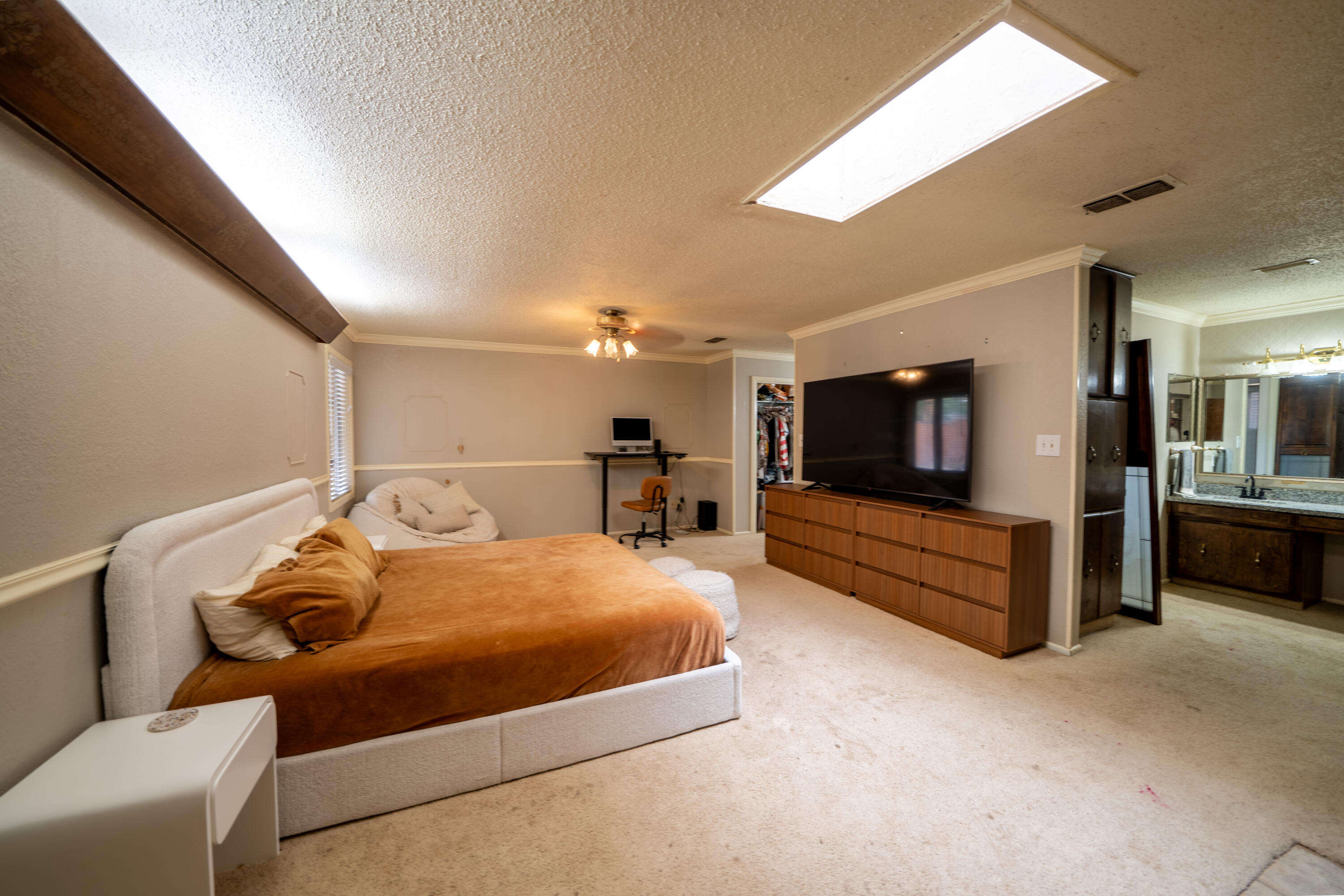 Furnished bedroom with a large bed, television, open closet, and adjoining double-vanity bathroom.