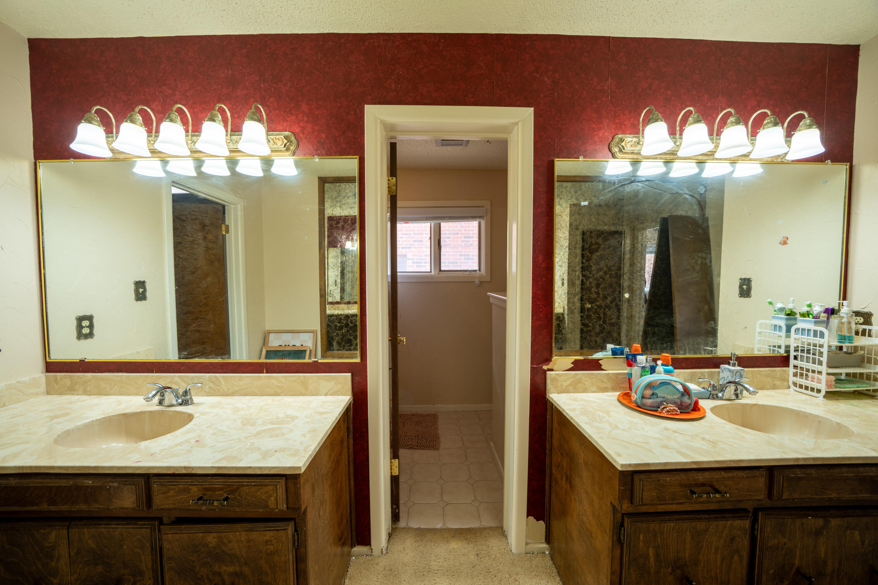 Bathroom with two wood vanities and large mirrors flanking a doorway to a tiled room.