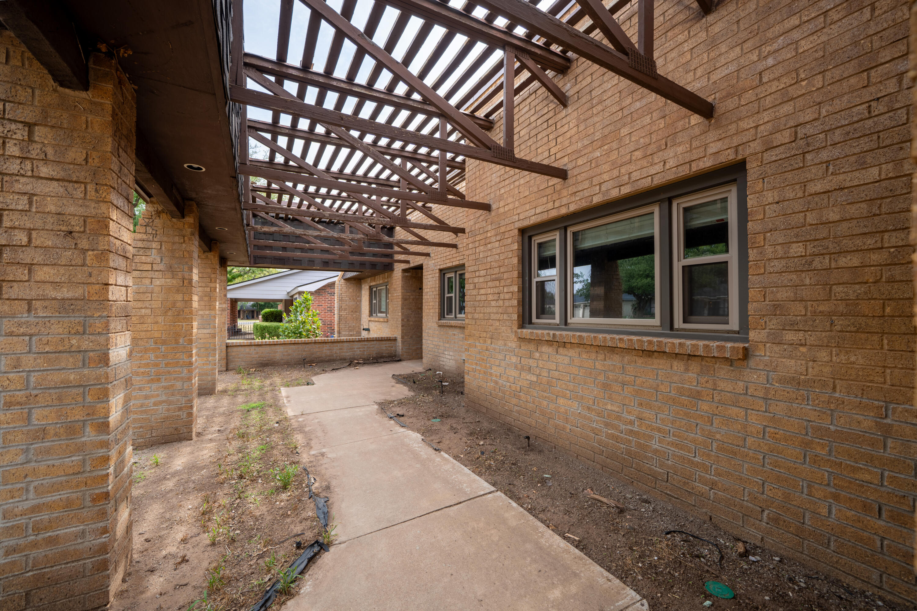 Brick courtyard with a concrete walkway beneath an open wooden pergola.