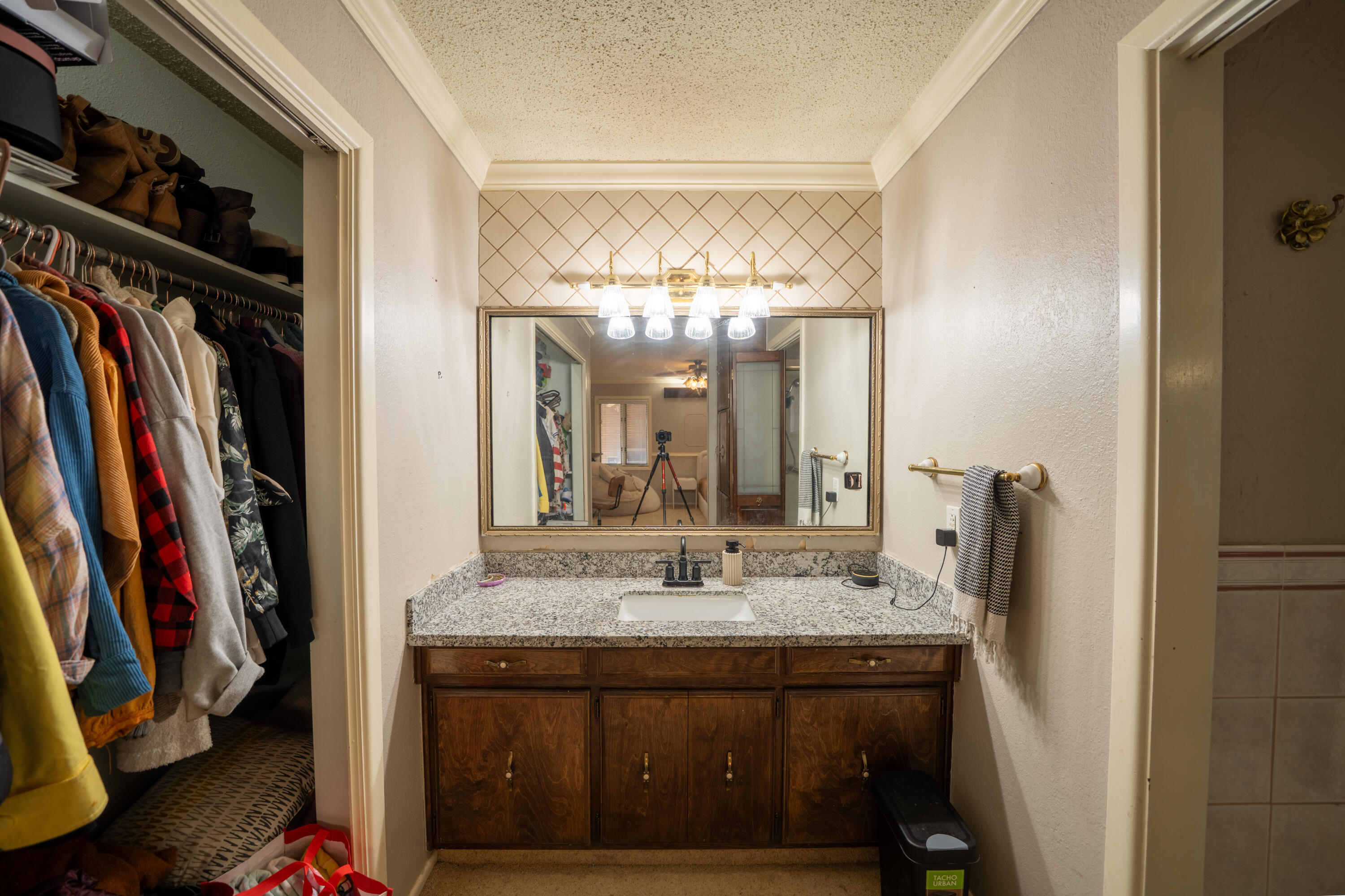 Bathroom vanity with a granite countertop and large mirror beside an open, clothing-filled closet.