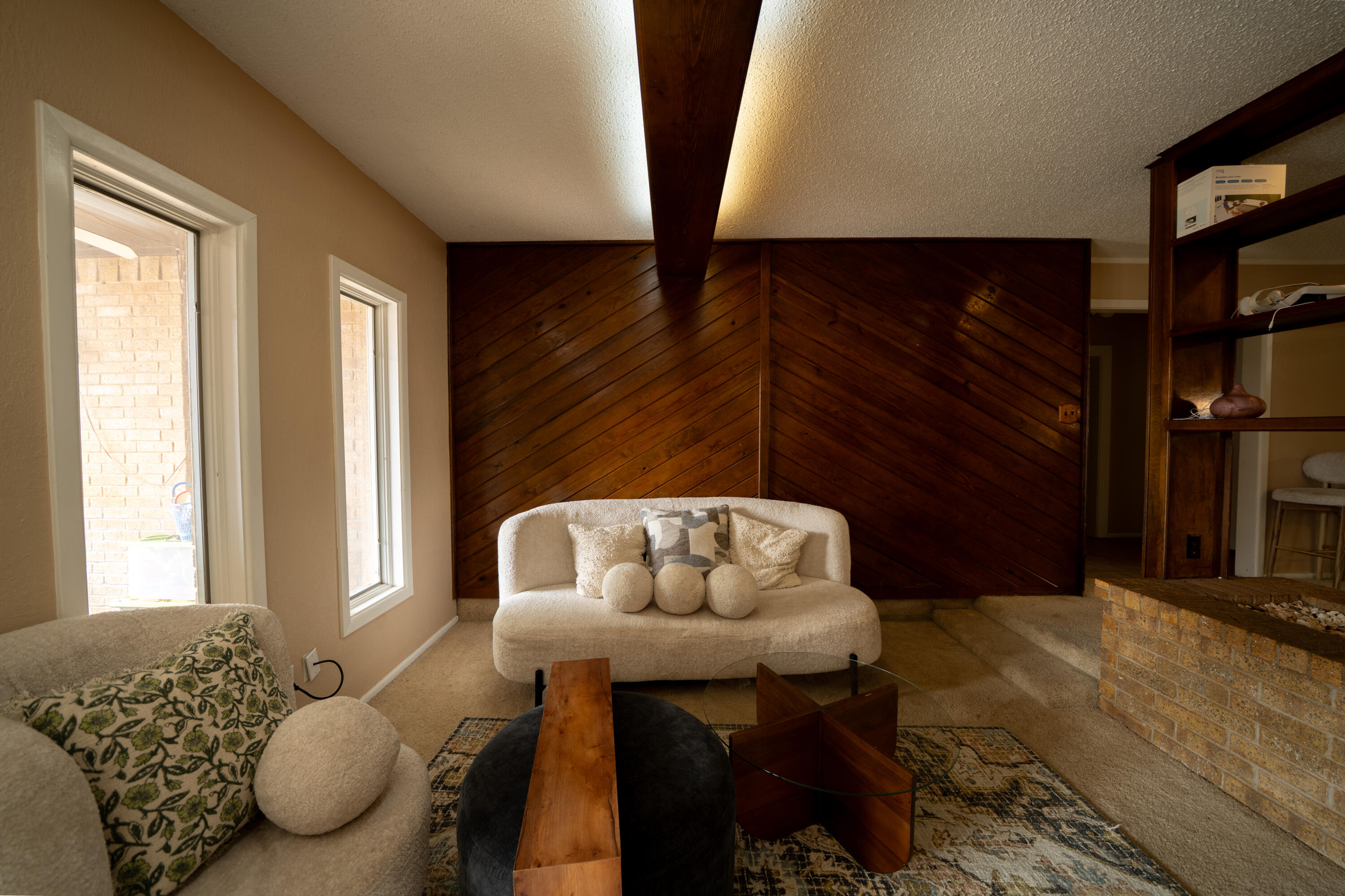 Living room with a dark wood accent wall, exposed ceiling beam, and cream seating.