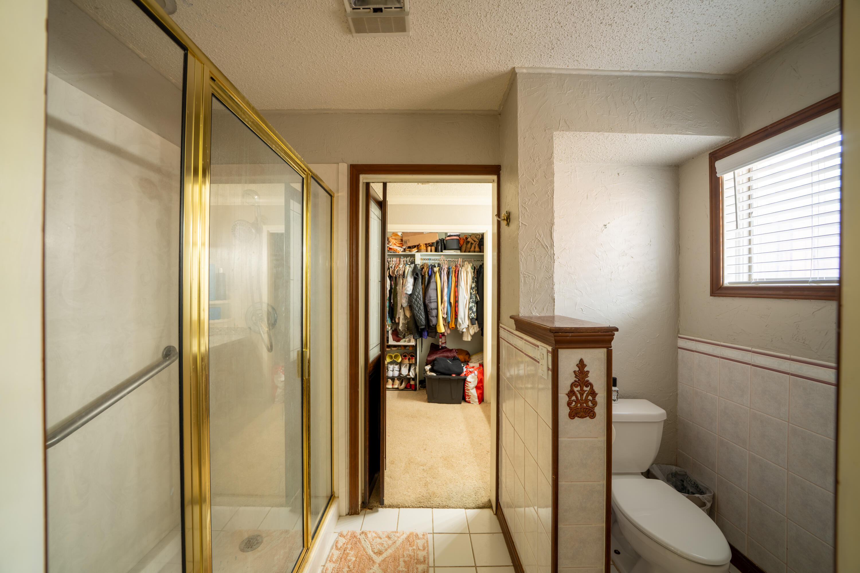 Bathroom with a glass shower, tiled half wall, and open doorway to a clothes-filled closet.