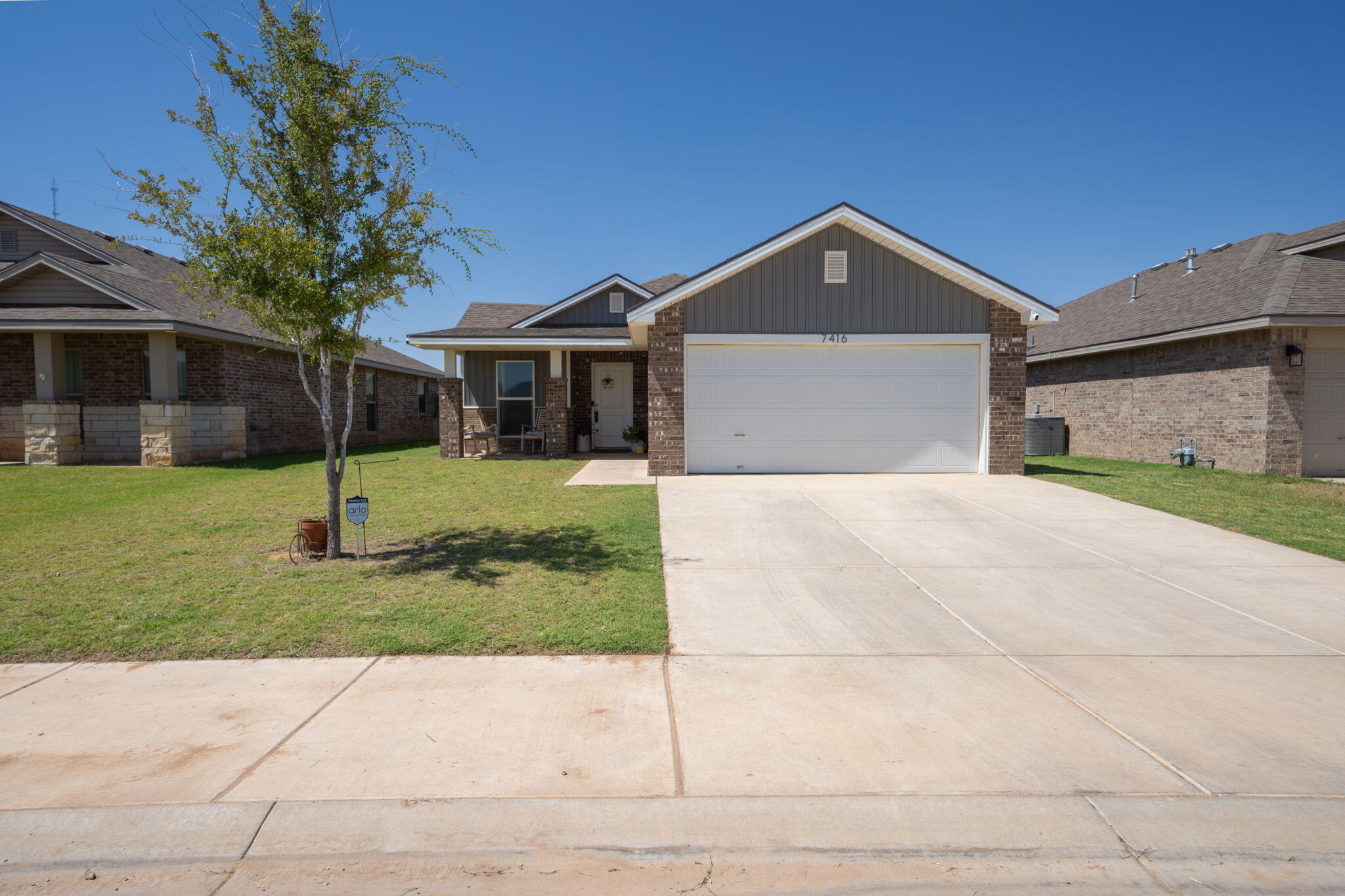 Brick house with a white double garage door, covered entry, lawn, and wide concrete driveway.