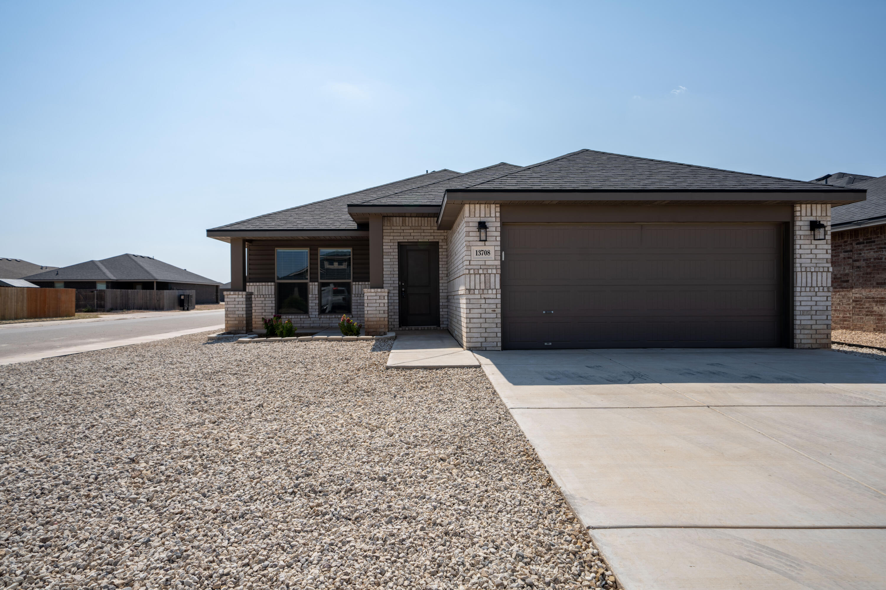 Single-story brick house with a wide two-car garage, concrete driveway, and gravel landscaping.