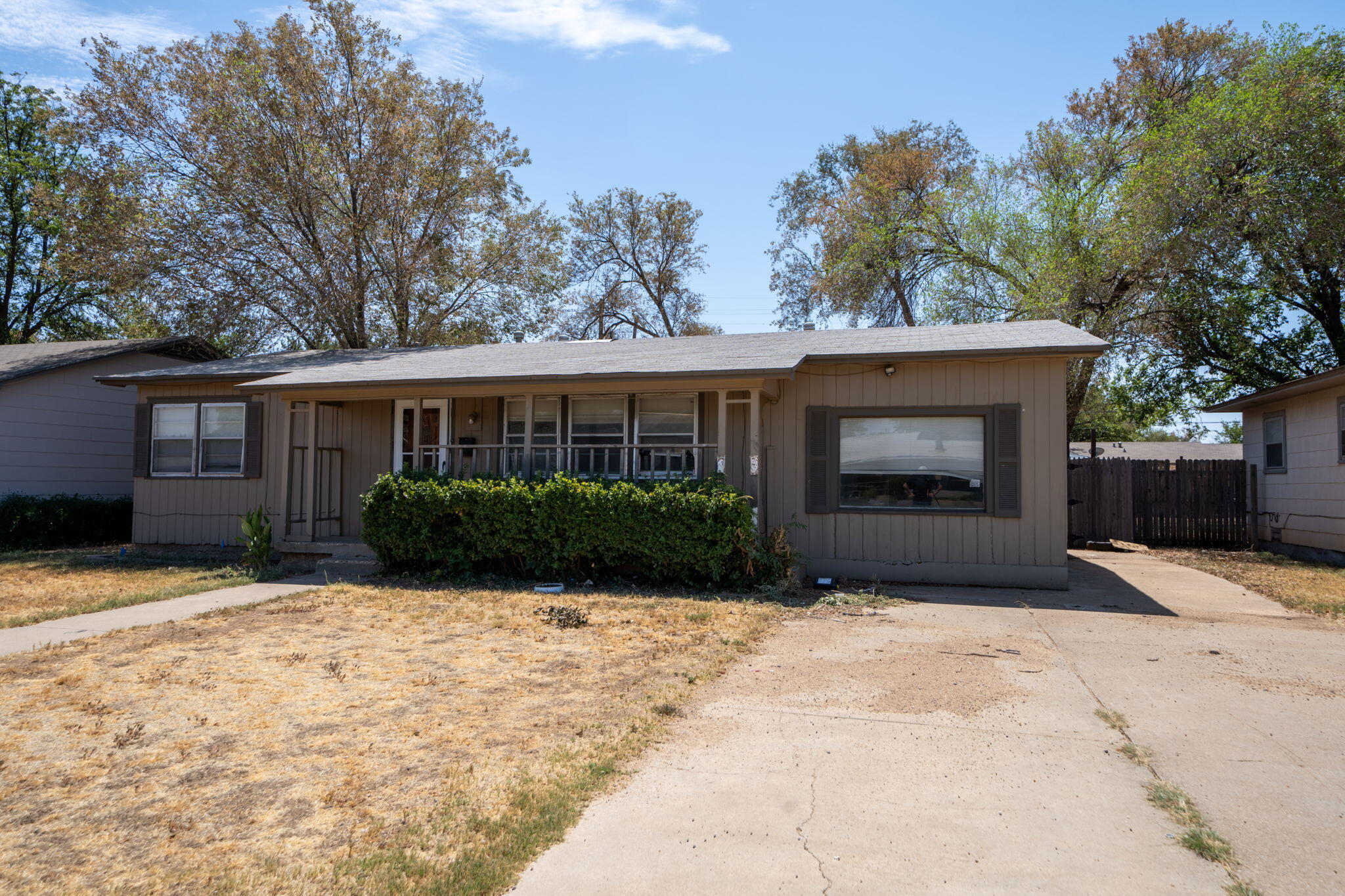 Single-story taupe house with a covered porch, large front window, and concrete driveway.
