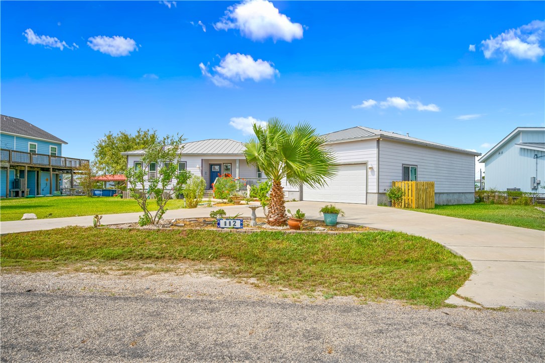 Single-story home with attached garage, metal roof, palm landscaping, and curved concrete driveway.