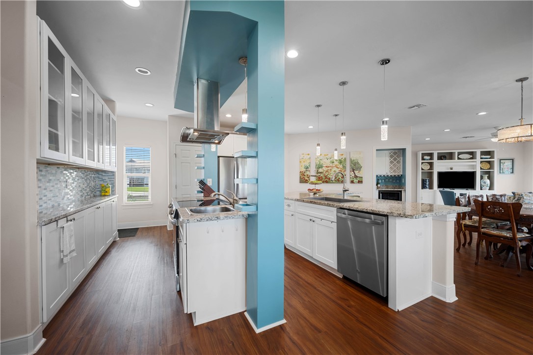 Open-plan kitchen with a granite island, white cabinetry, mosaic backsplash, and turquoise column.