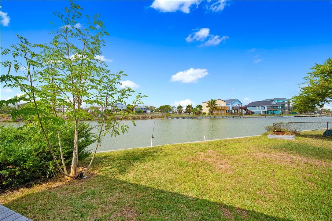 Waterfront yard beside a canal, with leafy trees and homes across the water.
