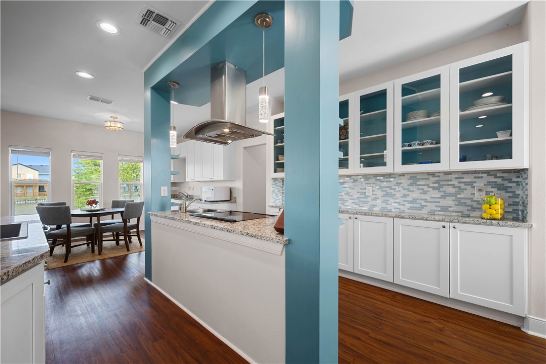 Open kitchen with turquoise accents, glass-front cabinets, mosaic backsplash, and adjoining dining area.