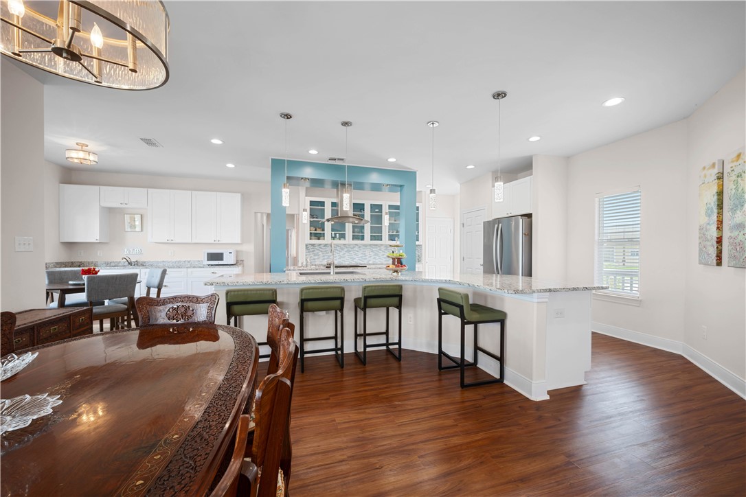 Open kitchen with a large granite island, green bar stools, turquoise accent wall, and hardwood floors.