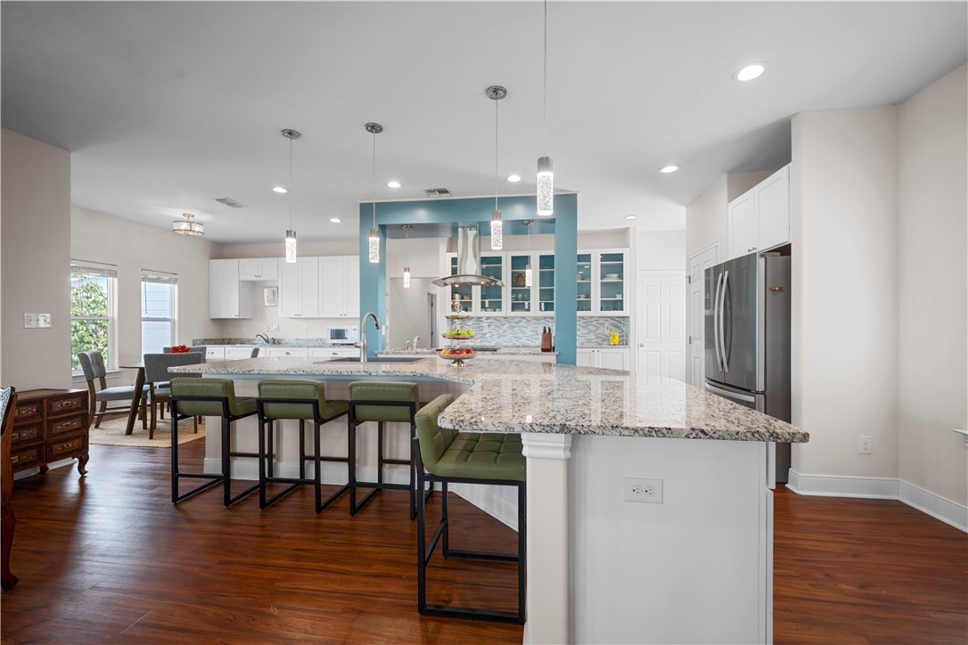 Open-plan kitchen with a large granite island, green bar stools, and white cabinetry.