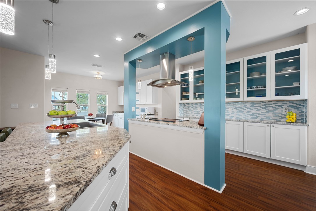 Modern kitchen with granite island, glass-front cabinets, blue tile backsplash, and turquoise framing.