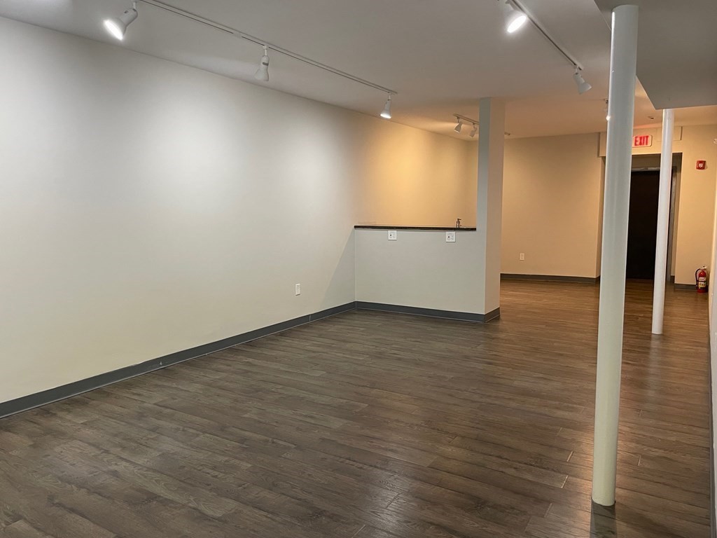 Vacant commercial interior with wood-look floors, track lighting, and white structural columns.