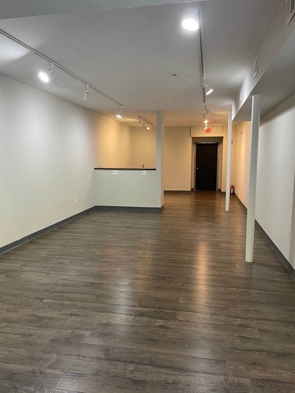 Vacant commercial interior with wood-look flooring, track lighting, and a counter near the rear.