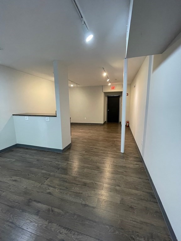 Vacant interior hallway with gray wood-look floors, a counter ledge, and a black door beneath an EXIT sign.