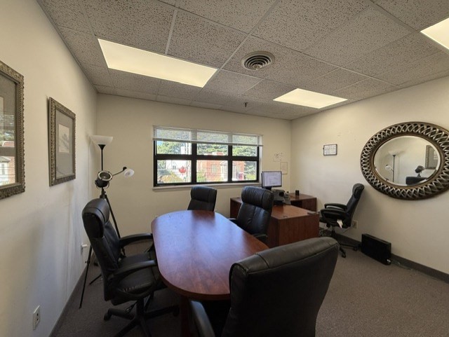Furnished conference room with an oval wooden table, black chairs, and a large round wall mirror.