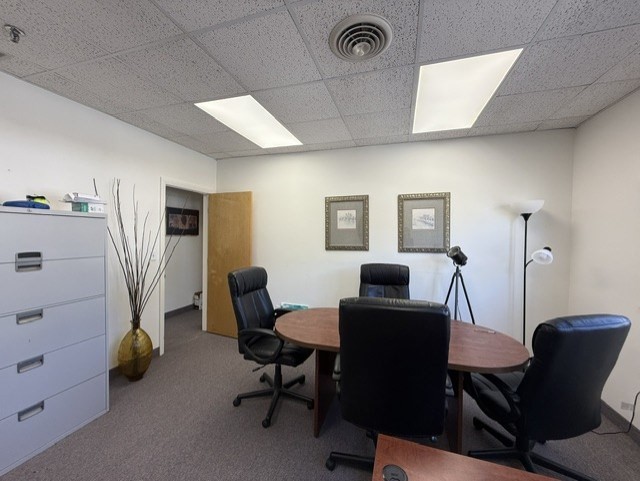 Office conference room with a round wooden table and black rolling chairs.