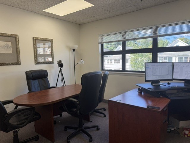 Office with two wooden desks, rolling chairs, and a wide window with blinds.