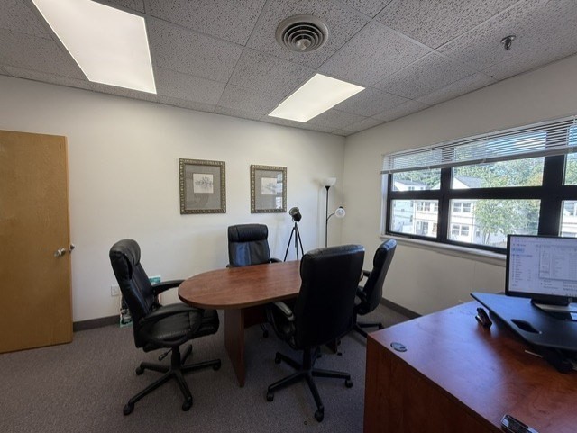 Furnished office conference room with an oval meeting table, rolling chairs, and large windows.