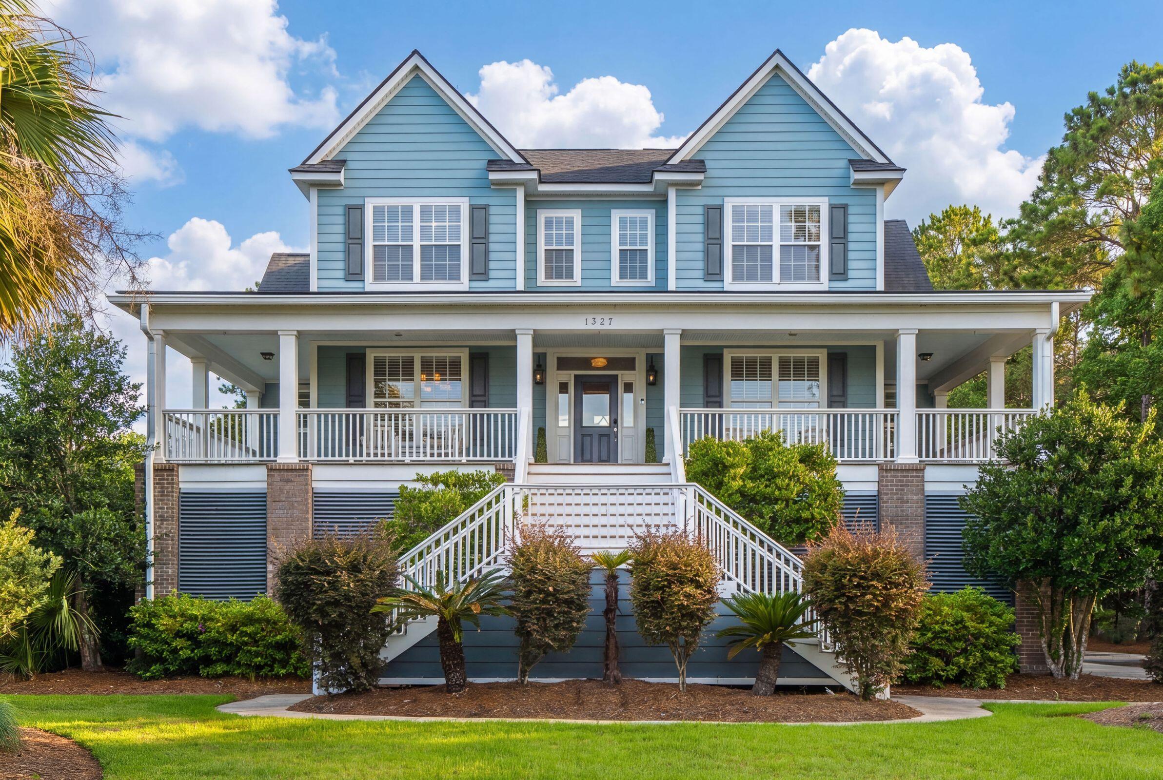 Blue two-story house with twin gables, a wide covered porch, and white front stairs.