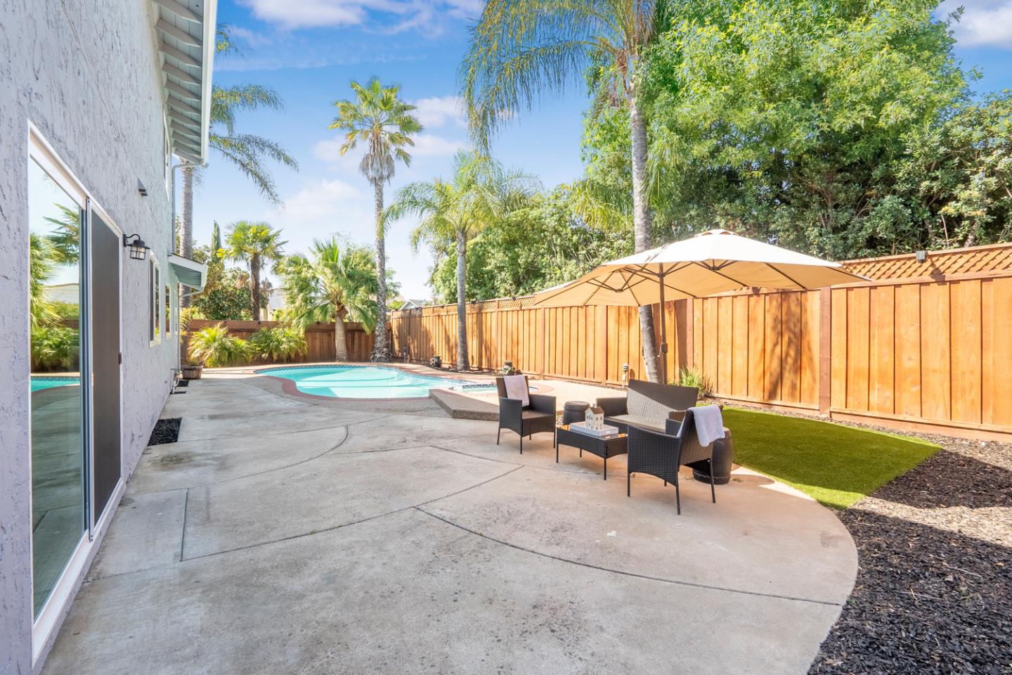 Backyard pool and concrete patio with umbrella-shaded seating and a wooden privacy fence.