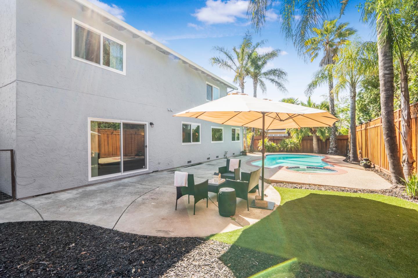 Backyard pool and patio with umbrella-shaded seating beside a two-story home.
