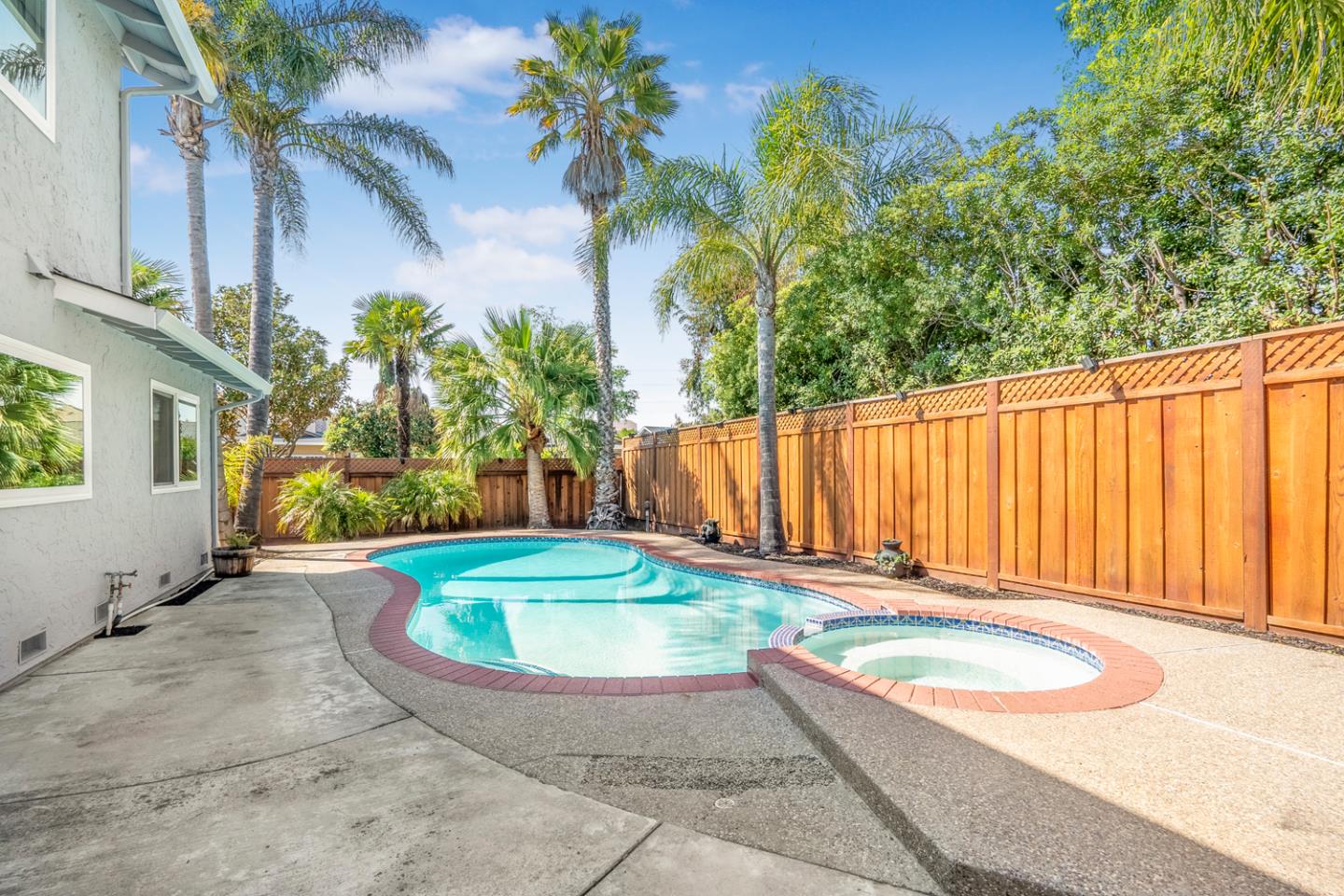 Backyard pool and circular spa beside a wooden privacy fence and palm trees.