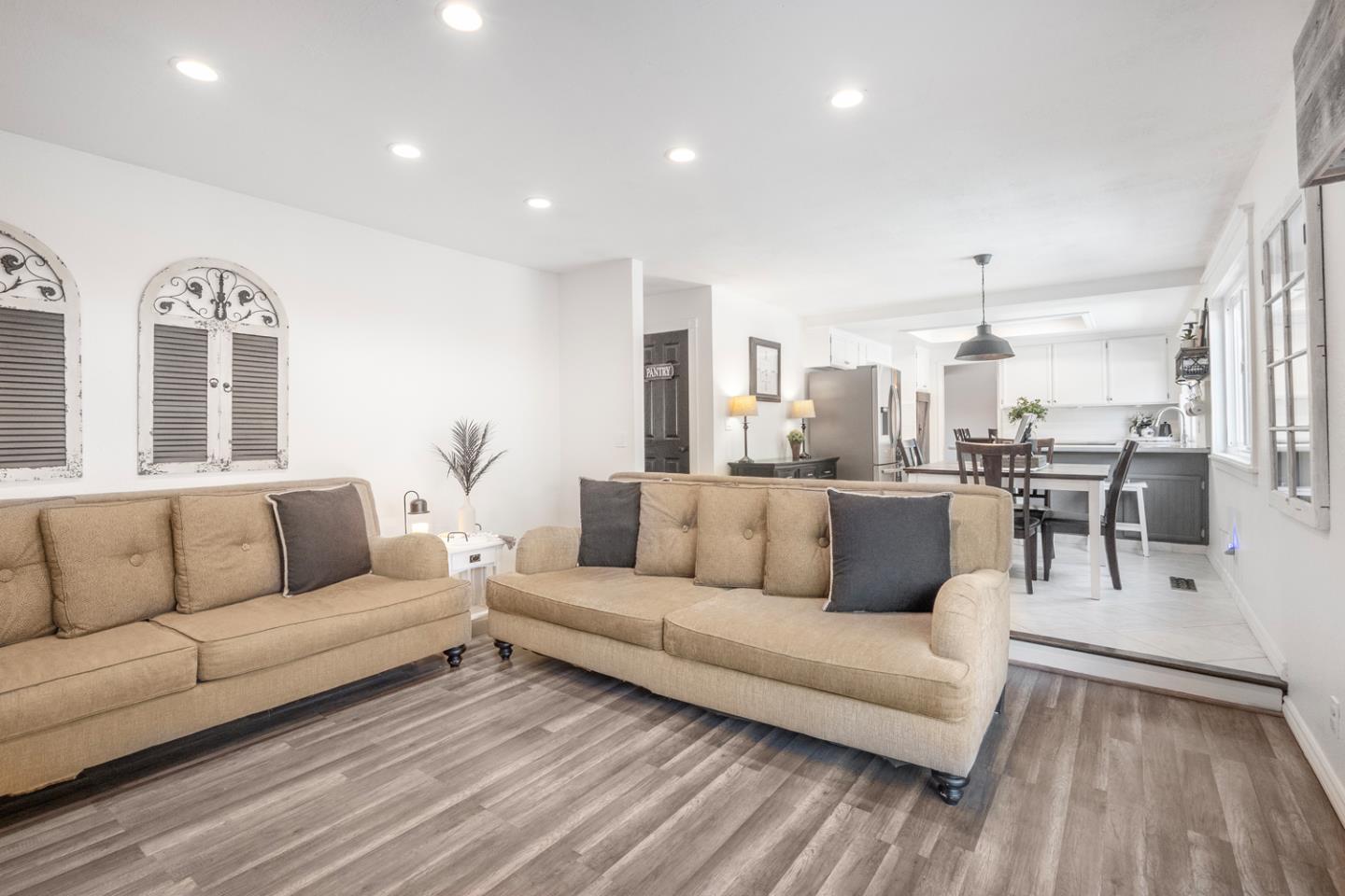 Furnished living room with beige sofas opening onto a dining area and white kitchen.