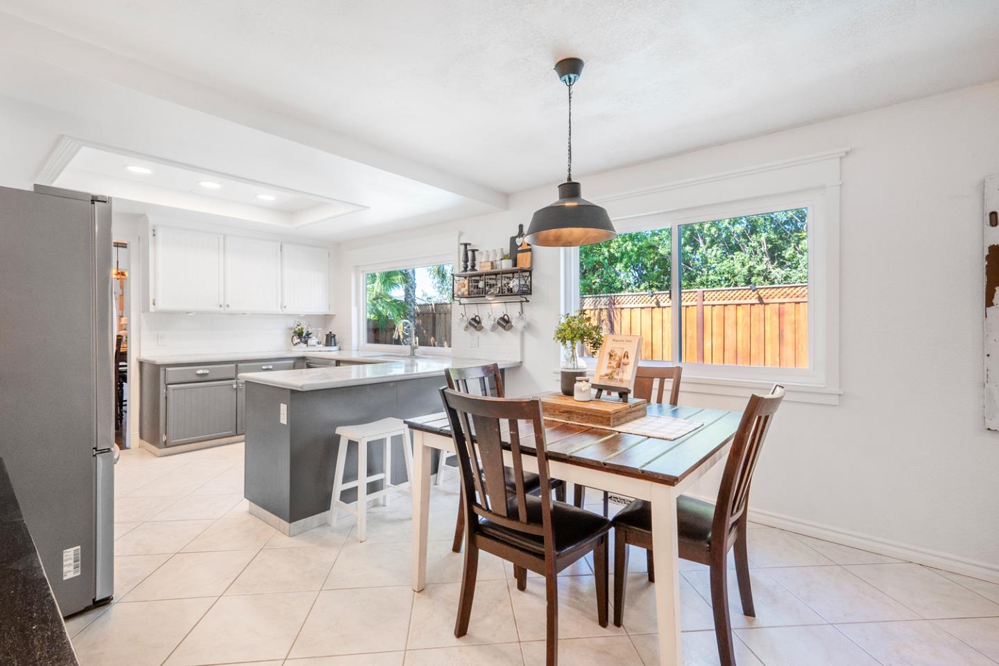 Kitchen and dining area with a gray island, dark wood table, and large backyard-facing windows.
