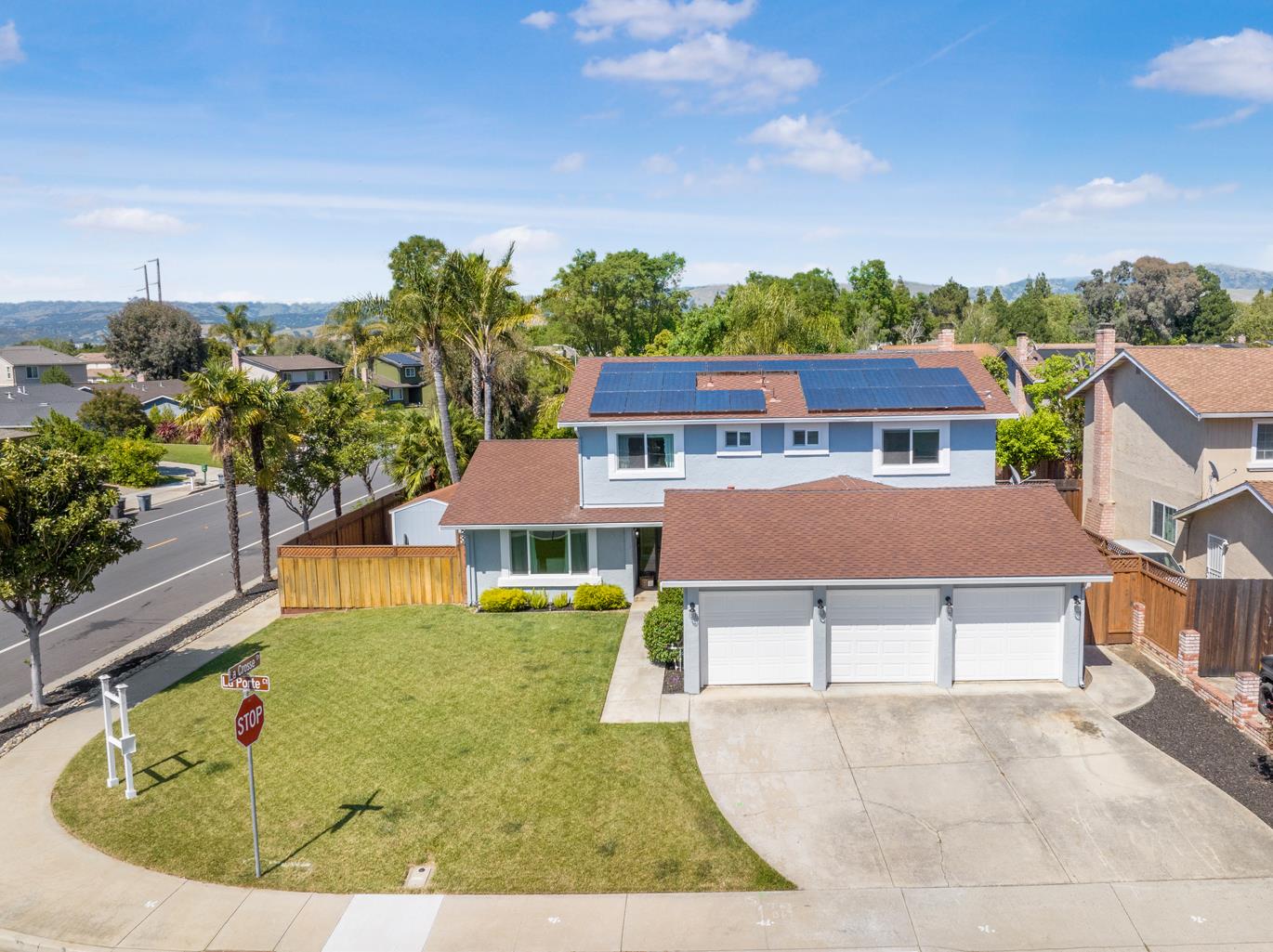 Two-story blue home with rooftop solar panels and a three-car garage on a landscaped corner lot.
