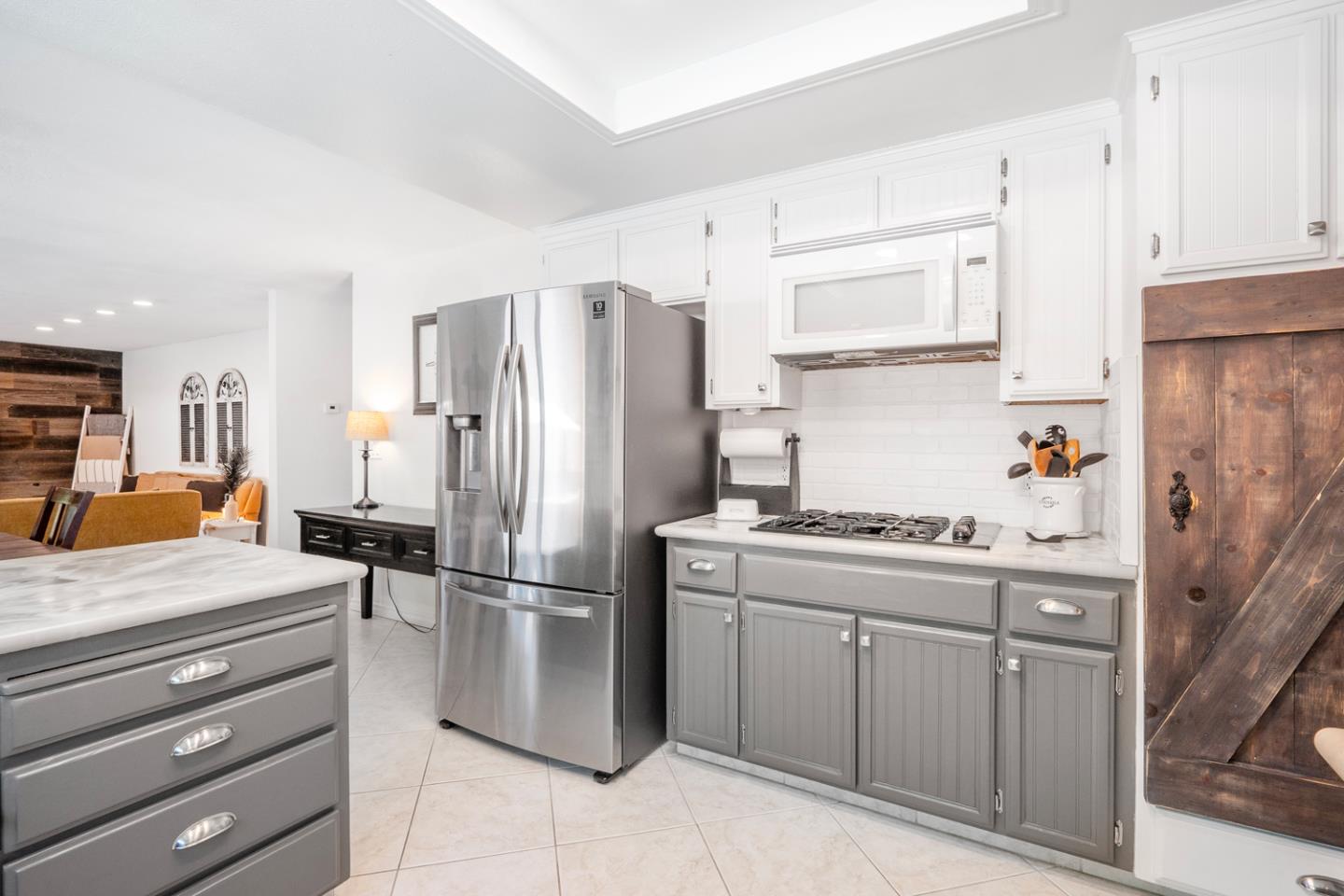 Kitchen with gray cabinets, a stainless-steel refrigerator, gas range, and adjoining living area.