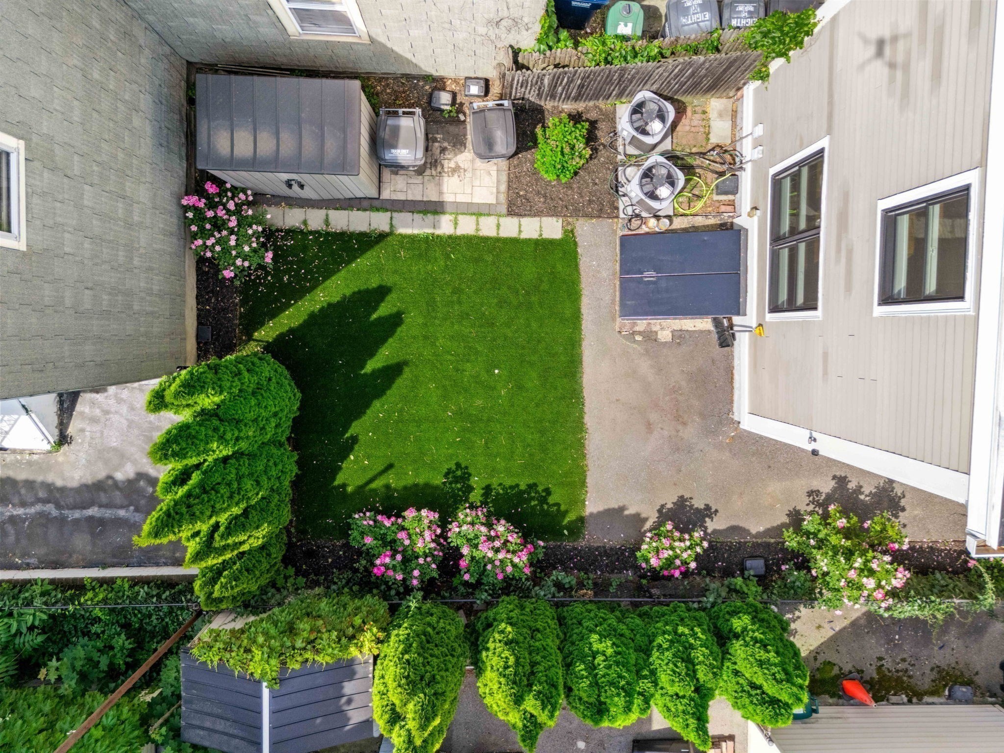 Aerial view of a landscaped courtyard with a green lawn, pink flowers, and paved paths.