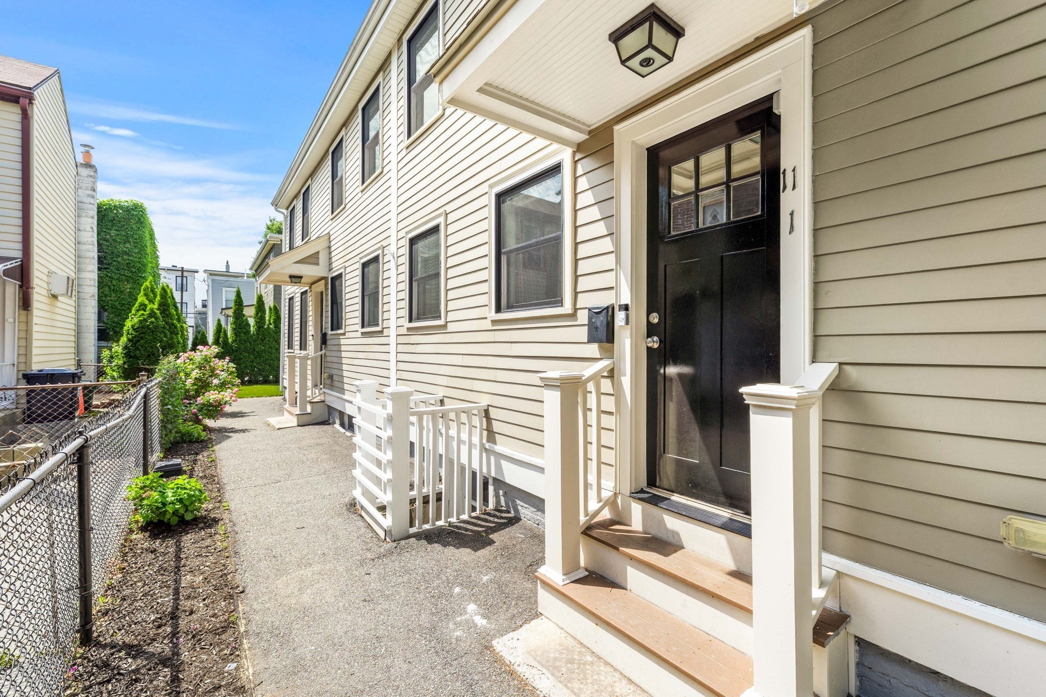 Townhouse entrance with a black door, white porch railings, and a flower-lined walkway.