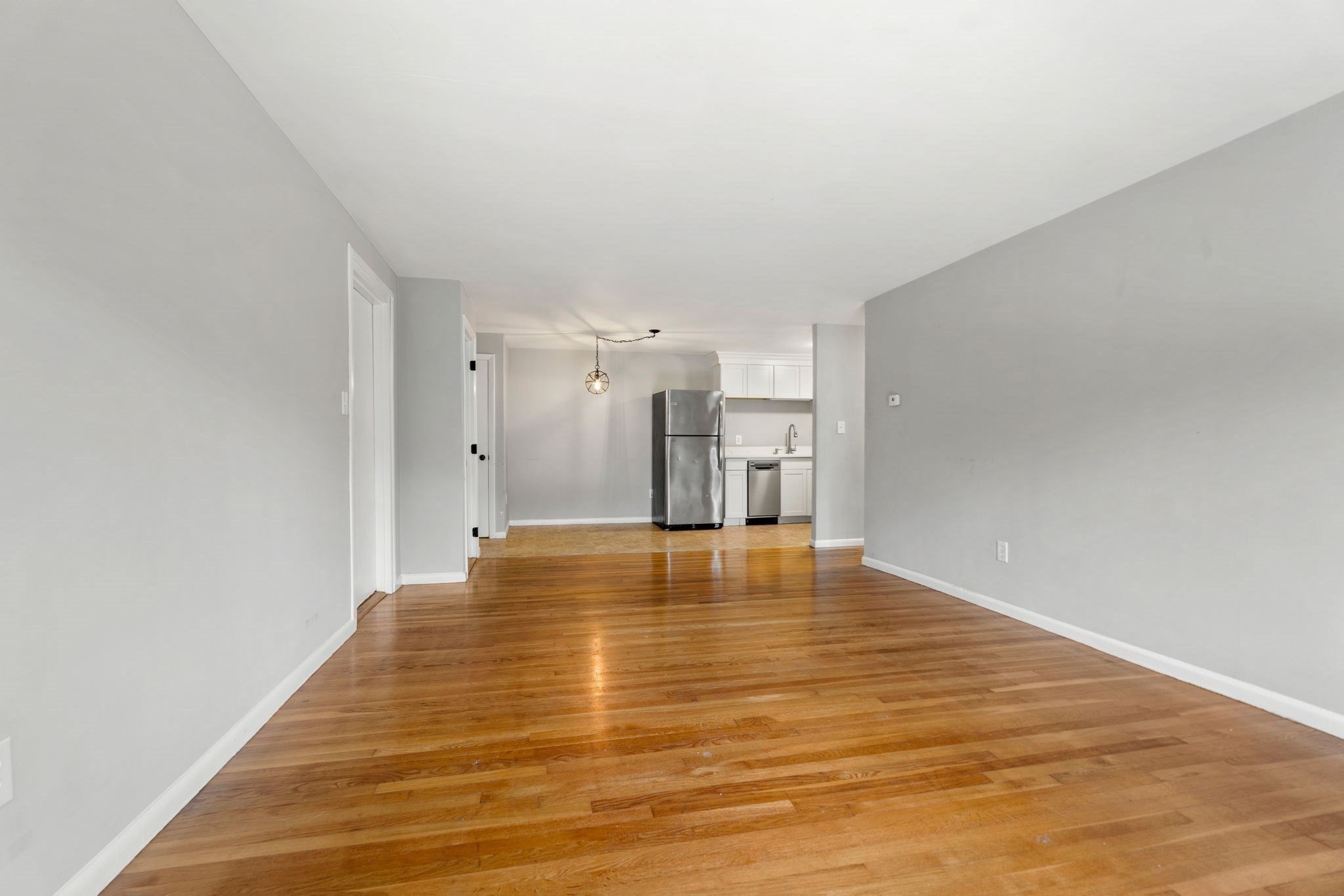 Empty living and dining area with hardwood floors and an open kitchen with stainless steel appliances.