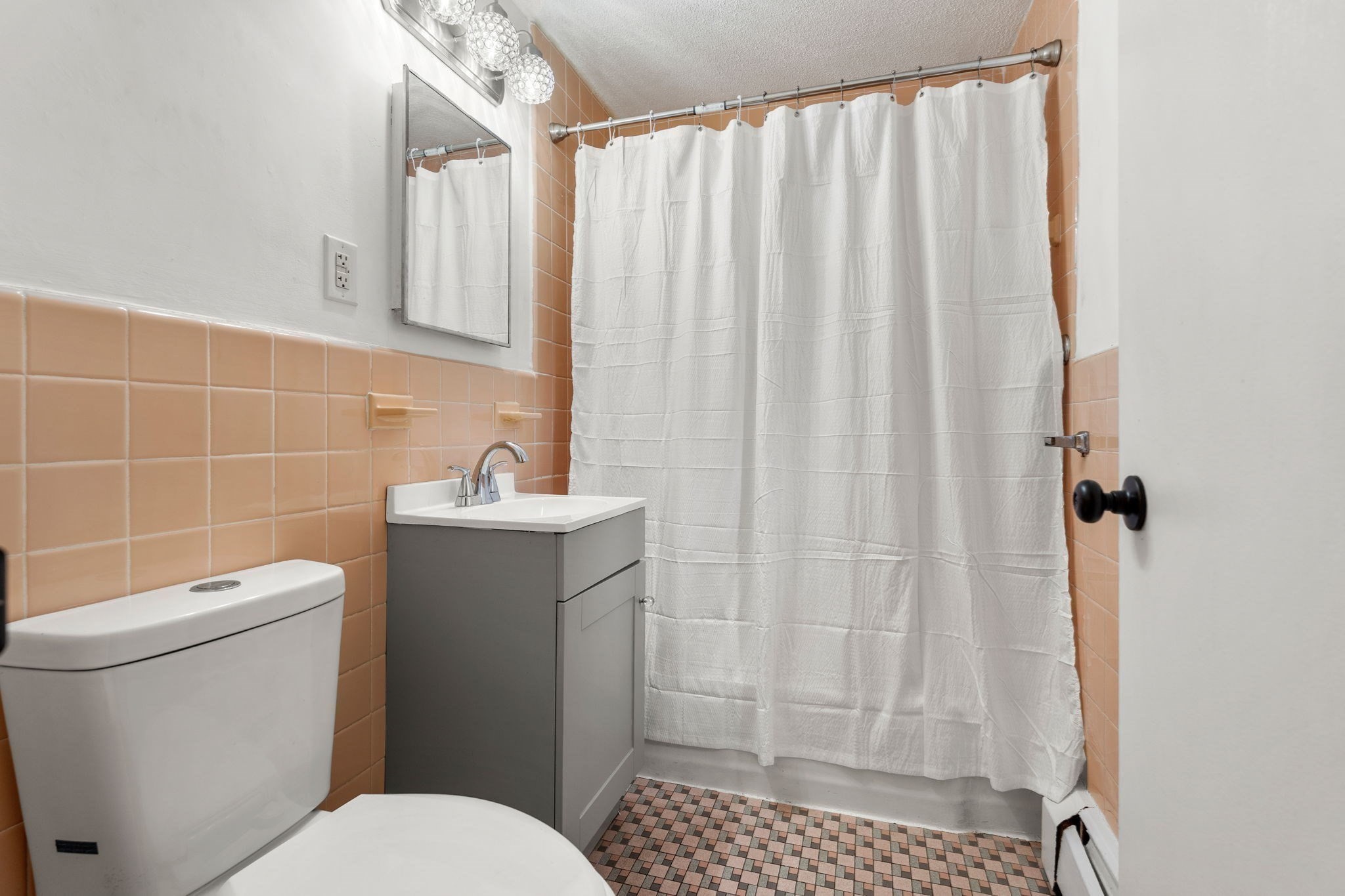 Bathroom with peach tile, gray vanity, white shower curtain, and mosaic floor.