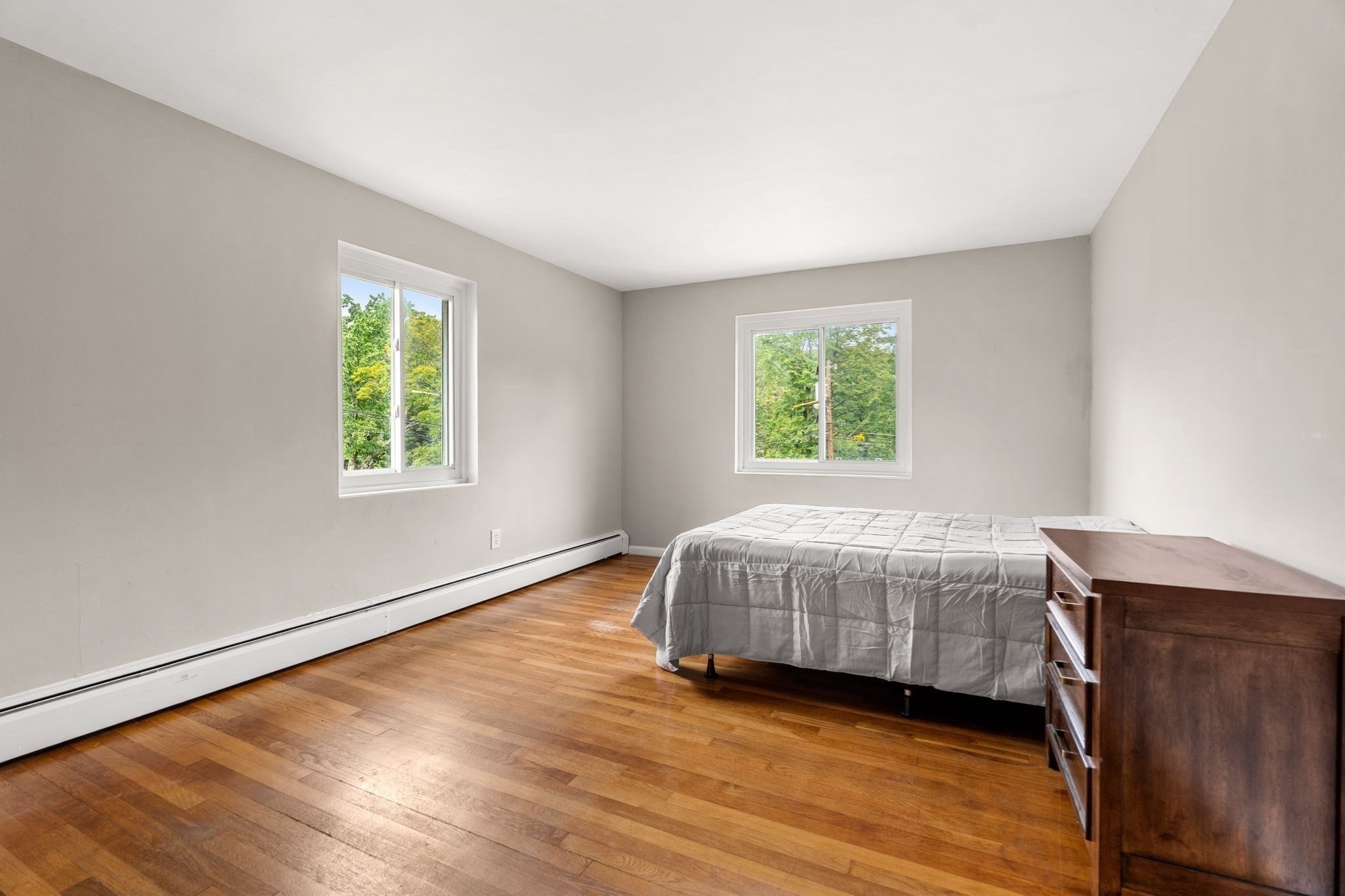 Bedroom with a bed, wooden dresser, two windows, and hardwood floors.