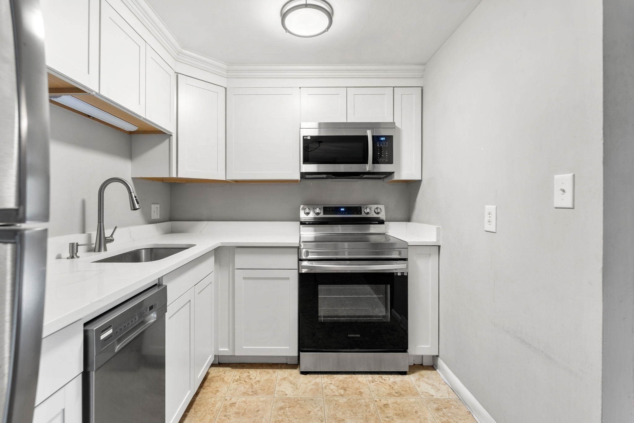 Compact kitchen with white cabinets, L-shaped counters, and stainless steel appliances.